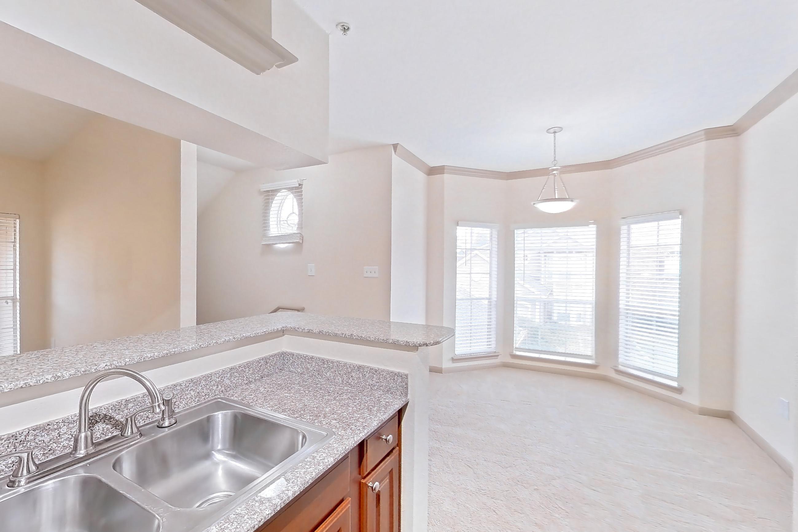 Kitchen with black appliances, dishwasher, electric range, in-unit laundry, light carpet, light countertops, light stone countertops, light wood-finish flooring, oven/range, refrigerator, and stainless steel appliances, Apartment 0425 at Marquis on Park Row