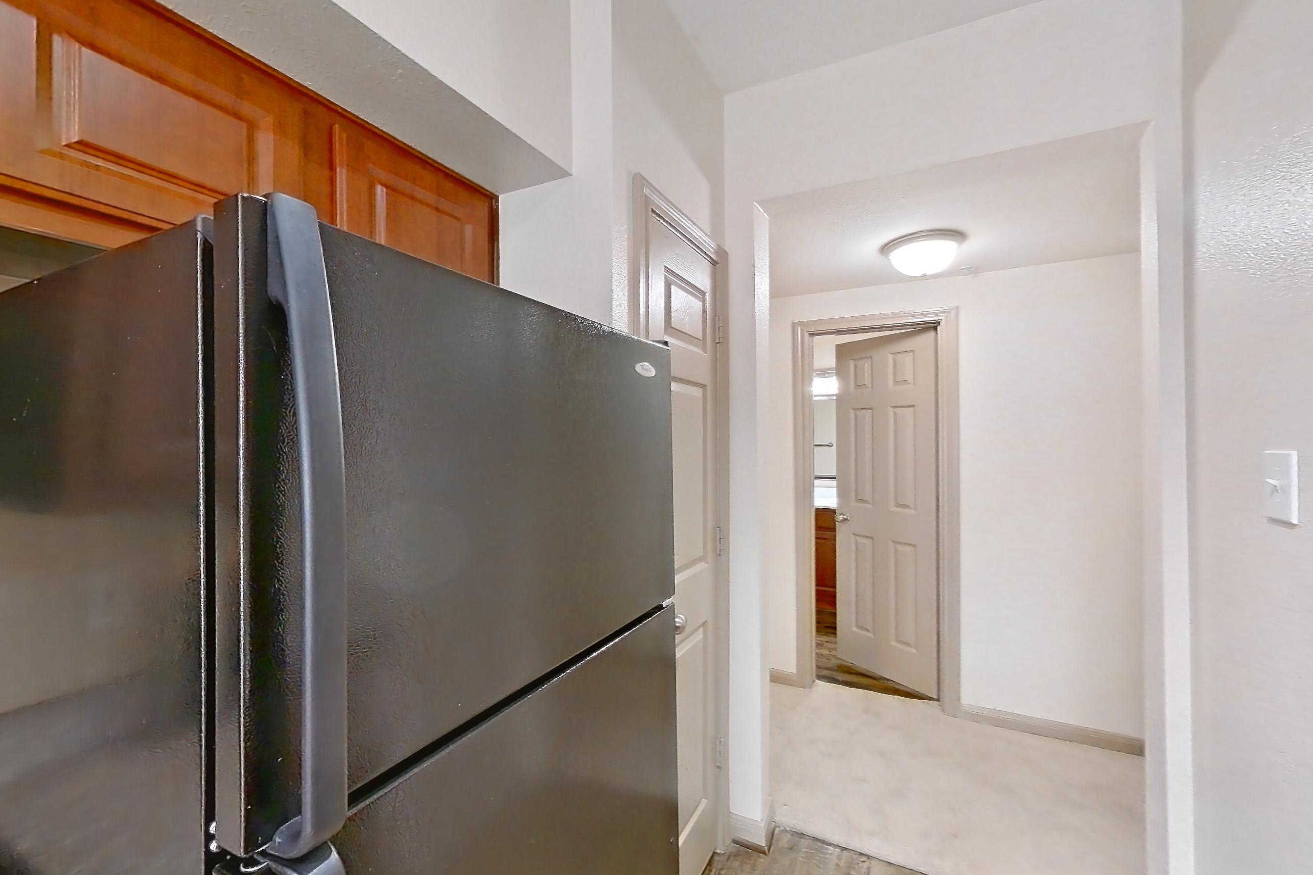 Kitchen with black appliances, dishwasher, electric range, in-unit laundry, light carpet, light countertops, light stone countertops, light wood-finish flooring, oven/range, refrigerator, and stainless steel appliances, Apartment 0425 at Marquis on Park Row