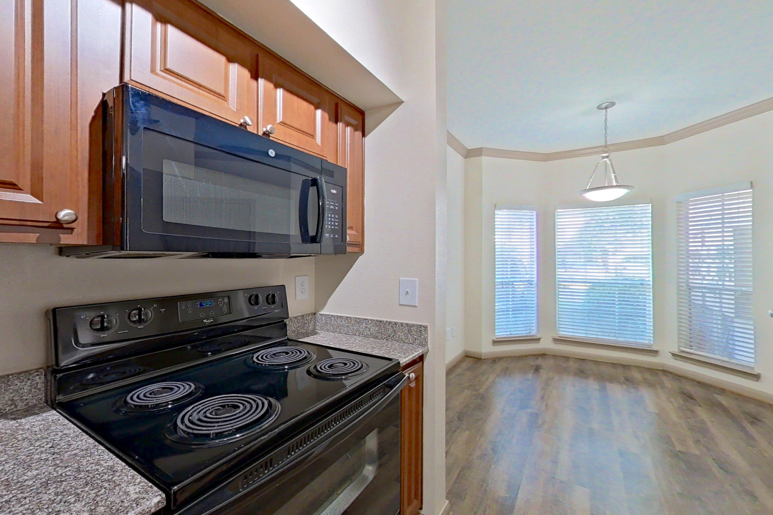 Kitchen with black appliances, dishwasher, electric range, light countertops, light stone countertops, light wood-finish flooring, microwave, oven/range, and refrigerator, Apartment 0618 at Marquis on Park Row