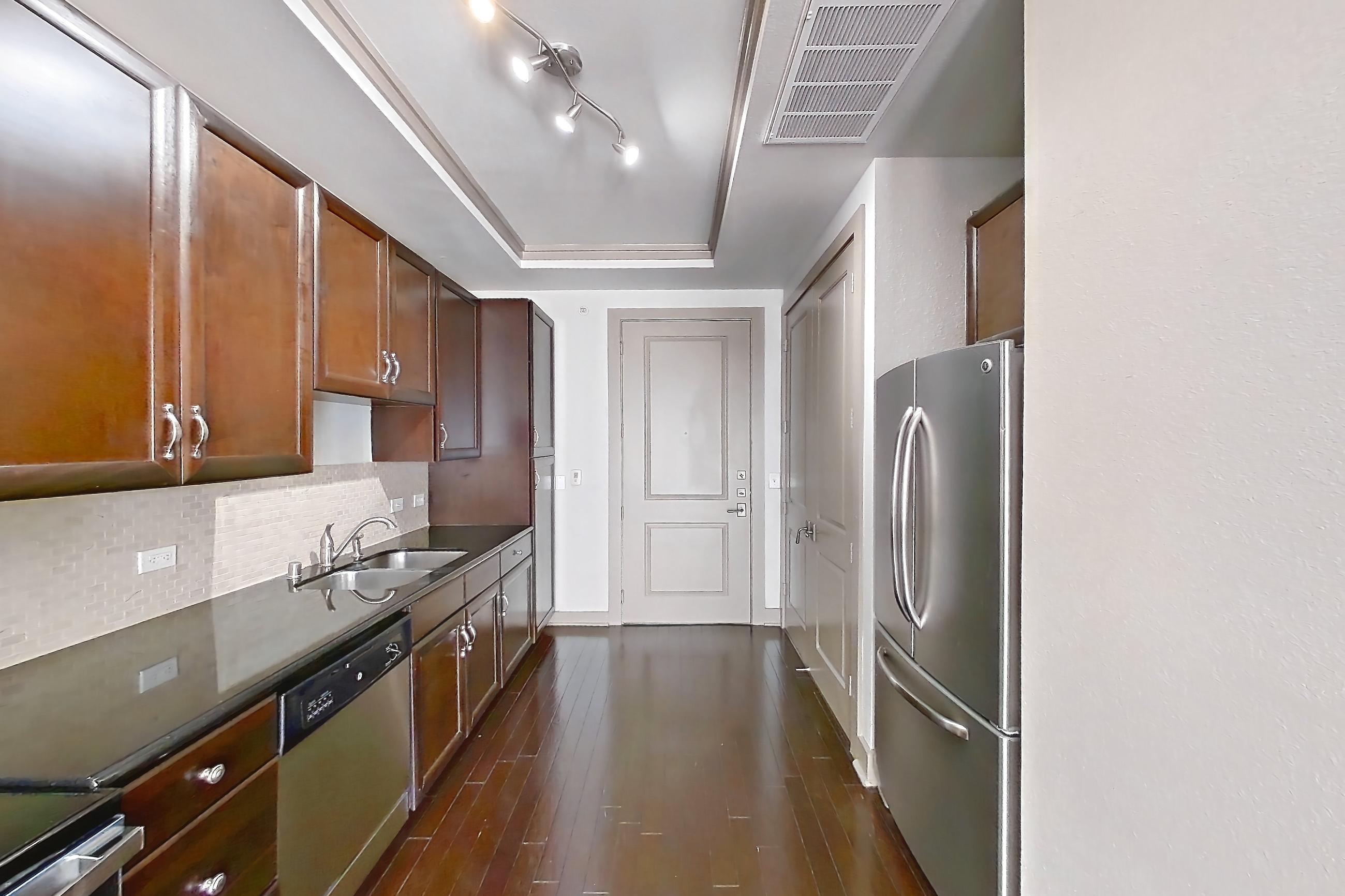 Kitchen with dark countertops, dark stone countertops, dark wood-finish flooring, dishwasher, electric range, microwave, oven/range, refrigerator, stainless steel appliances, and wood-finish flooring, Apartment 309 at The Marquis of State Thomas