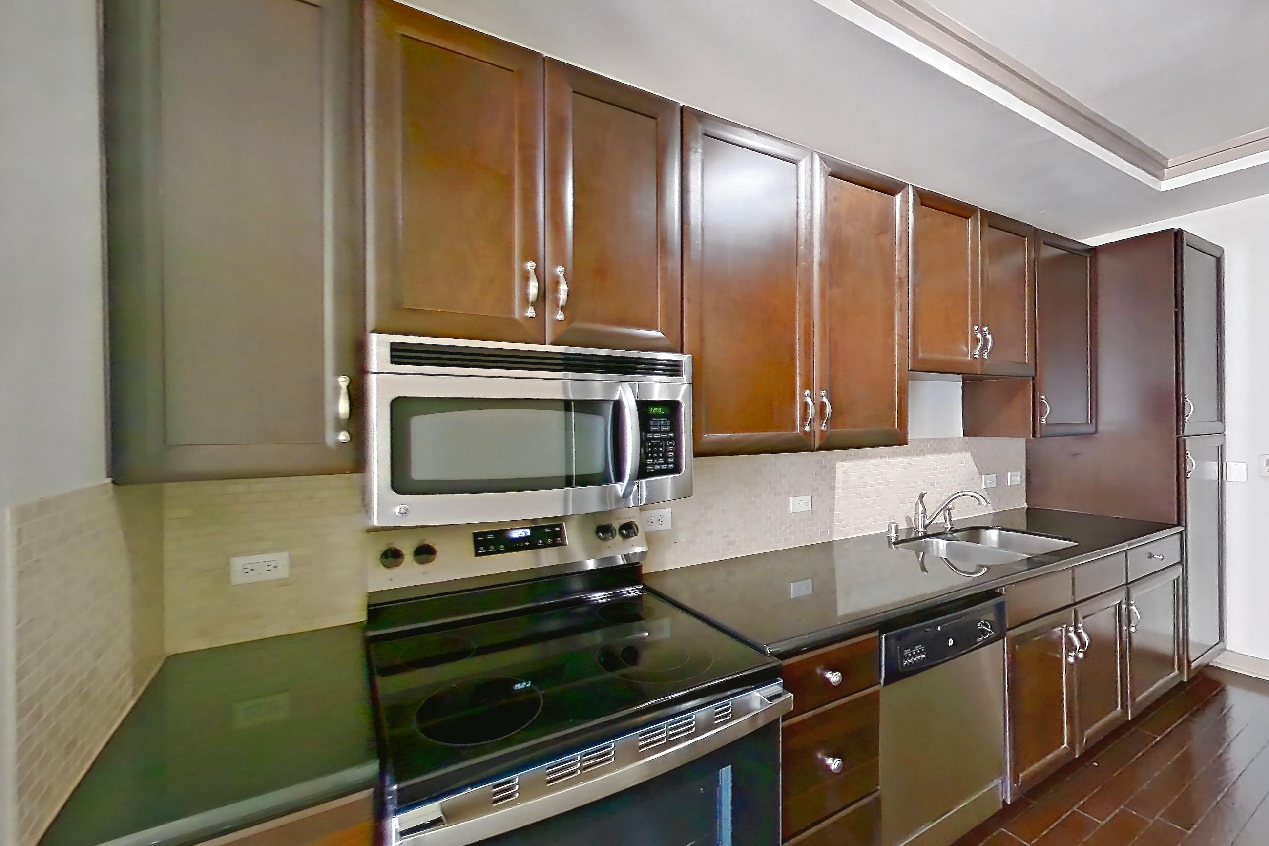 Kitchen with dark countertops, dark stone countertops, dark wood-finish flooring, dishwasher, electric range, microwave, oven/range, refrigerator, stainless steel appliances, and wood-finish flooring, Apartment 309 at The Marquis of State Thomas