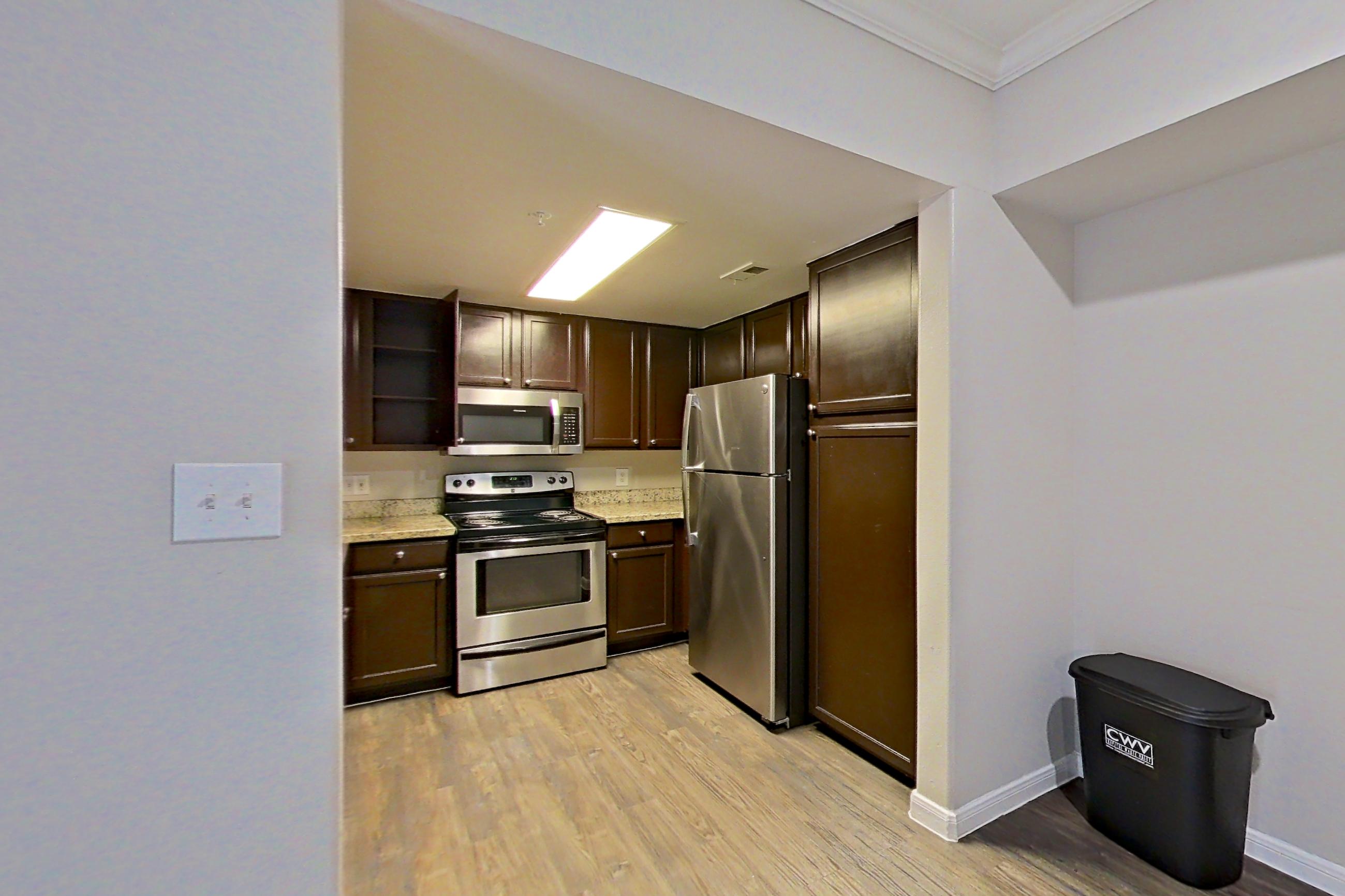 Dining room with dark wood-finish flooring, electric range, fireplace, light stone countertops, light wood-finish flooring, oven/range, refrigerator, and stainless steel appliances, Apartment 0233 at Marquis on Westheimer