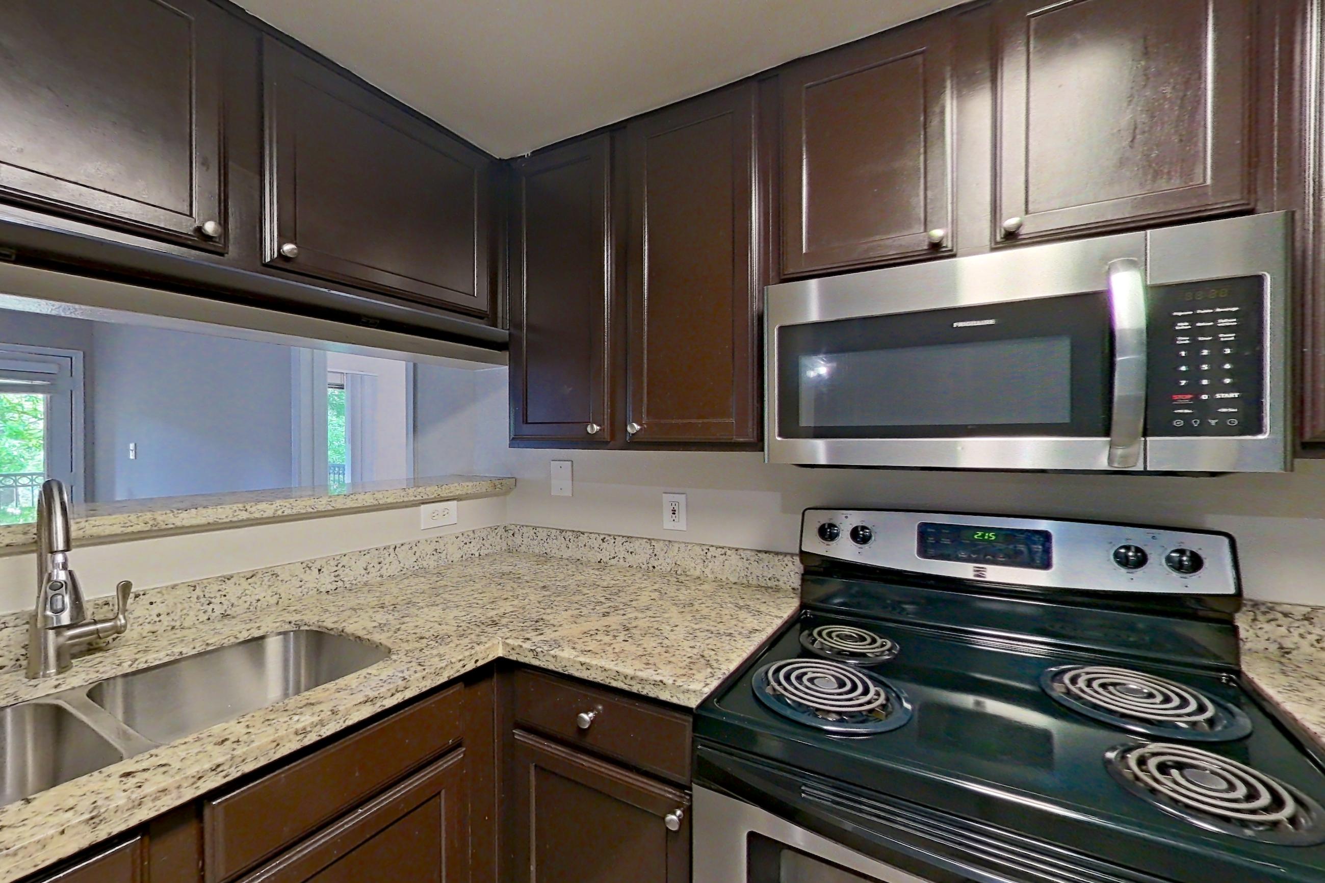 Kitchen with dark wood-finish flooring, dishwasher, electric range, light stone countertops, light wood-finish flooring, microwave, oven/range, and stainless steel appliances, Apartment 0233 at Marquis on Westheimer