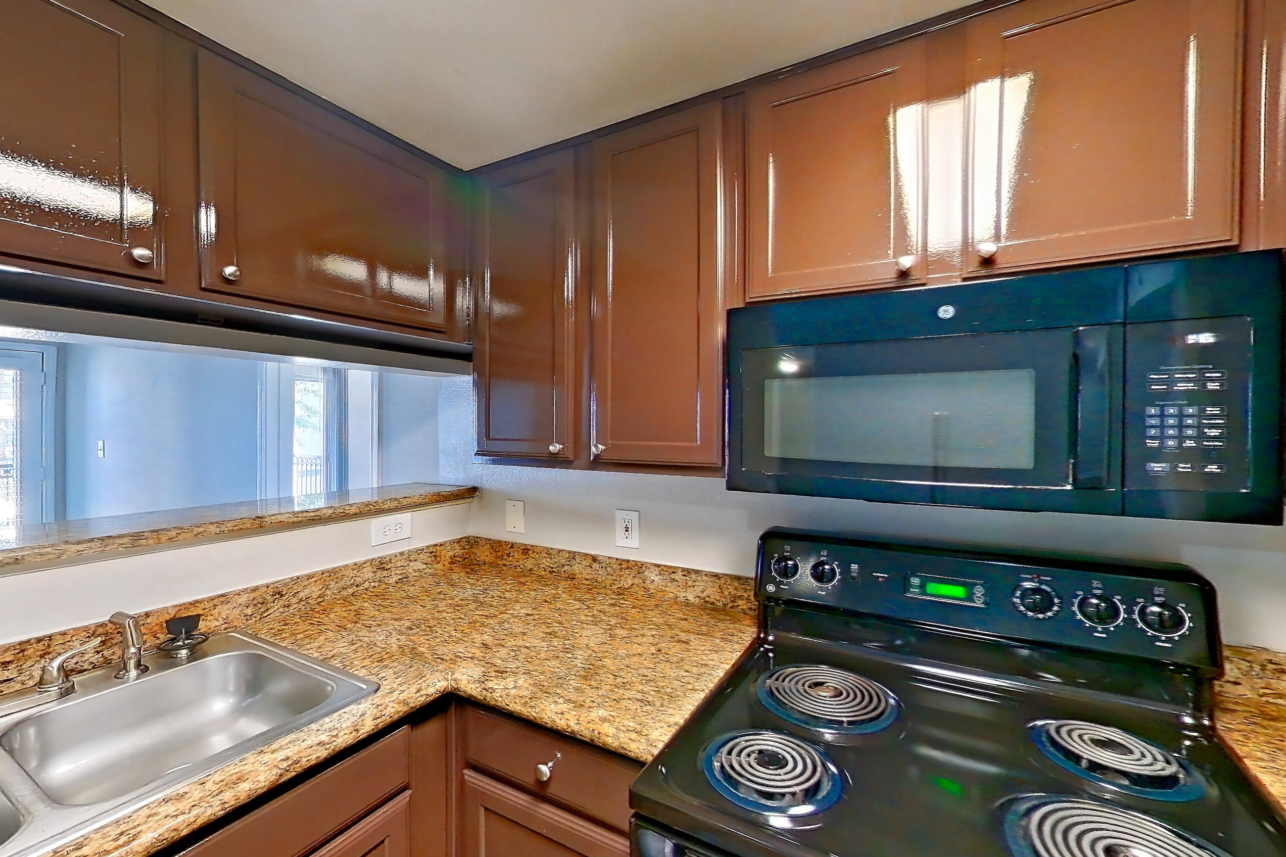 Kitchen with black appliances, cooktop, dark wood-finish flooring, dishwasher, electric range, light countertops, light stone countertops, light wood-finish flooring, microwave, oven/range, and stainless steel appliances, Apartment 0323 at Marquis on Westheimer