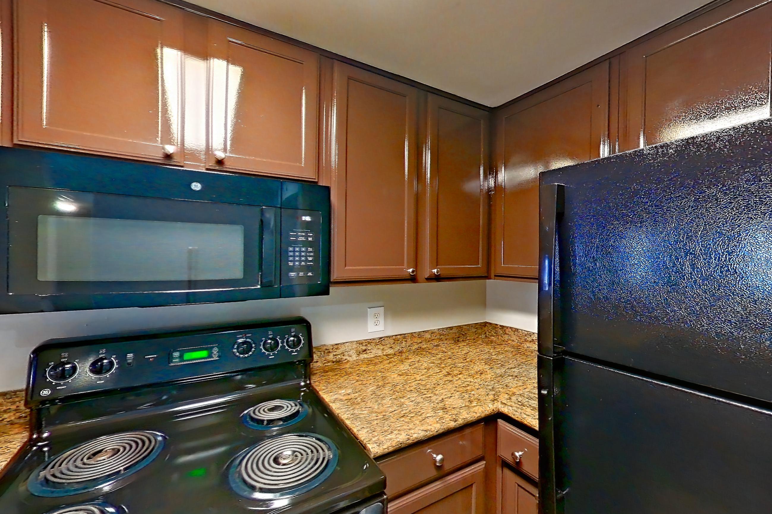 Kitchen with black appliances, cooktop, dark wood-finish flooring, dishwasher, electric range, light countertops, light stone countertops, light wood-finish flooring, microwave, oven/range, and stainless steel appliances, Apartment 0323 at Marquis on Westheimer