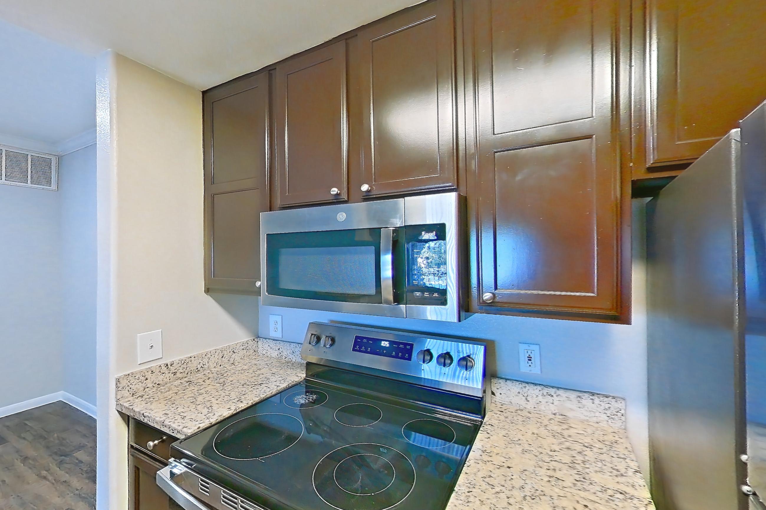 Kitchen with dishwasher, electric range, light stone countertops, light wood-finish flooring, microwave, oven/range, refrigerator, and stainless steel appliances, Apartment 0335 at Marquis on Westheimer