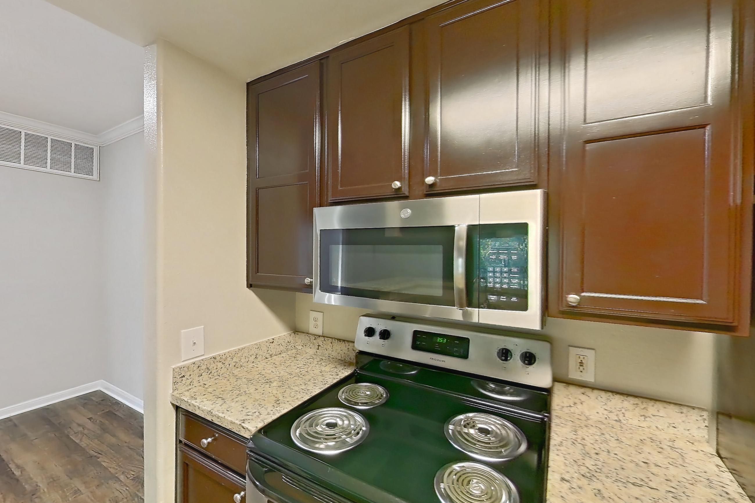 Kitchen with dishwasher, electric range, light stone countertops, light wood-finish flooring, microwave, oven/range, refrigerator, stainless steel appliances, and white appliances, Apartment 0433 at Marquis on Westheimer