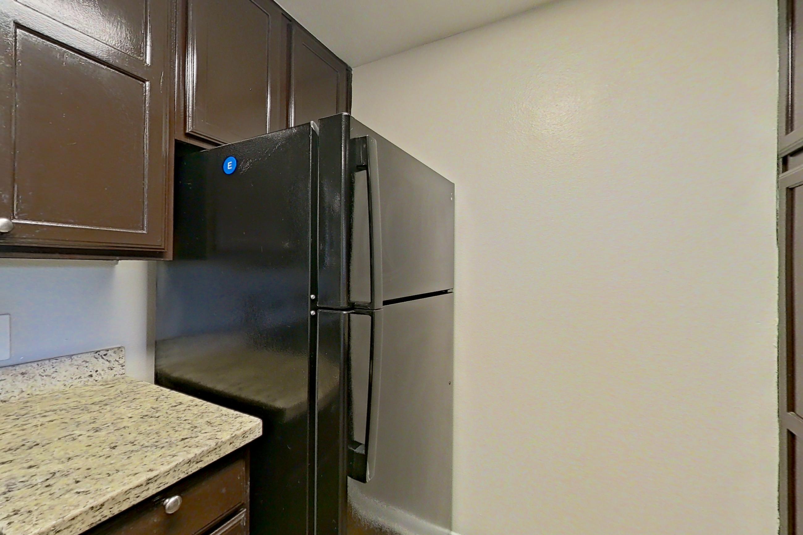 Kitchen with dark wood-finish flooring, dishwasher, electric range, light stone countertops, refrigerator, and stainless steel appliances, Apartment 0525 at Marquis on Westheimer