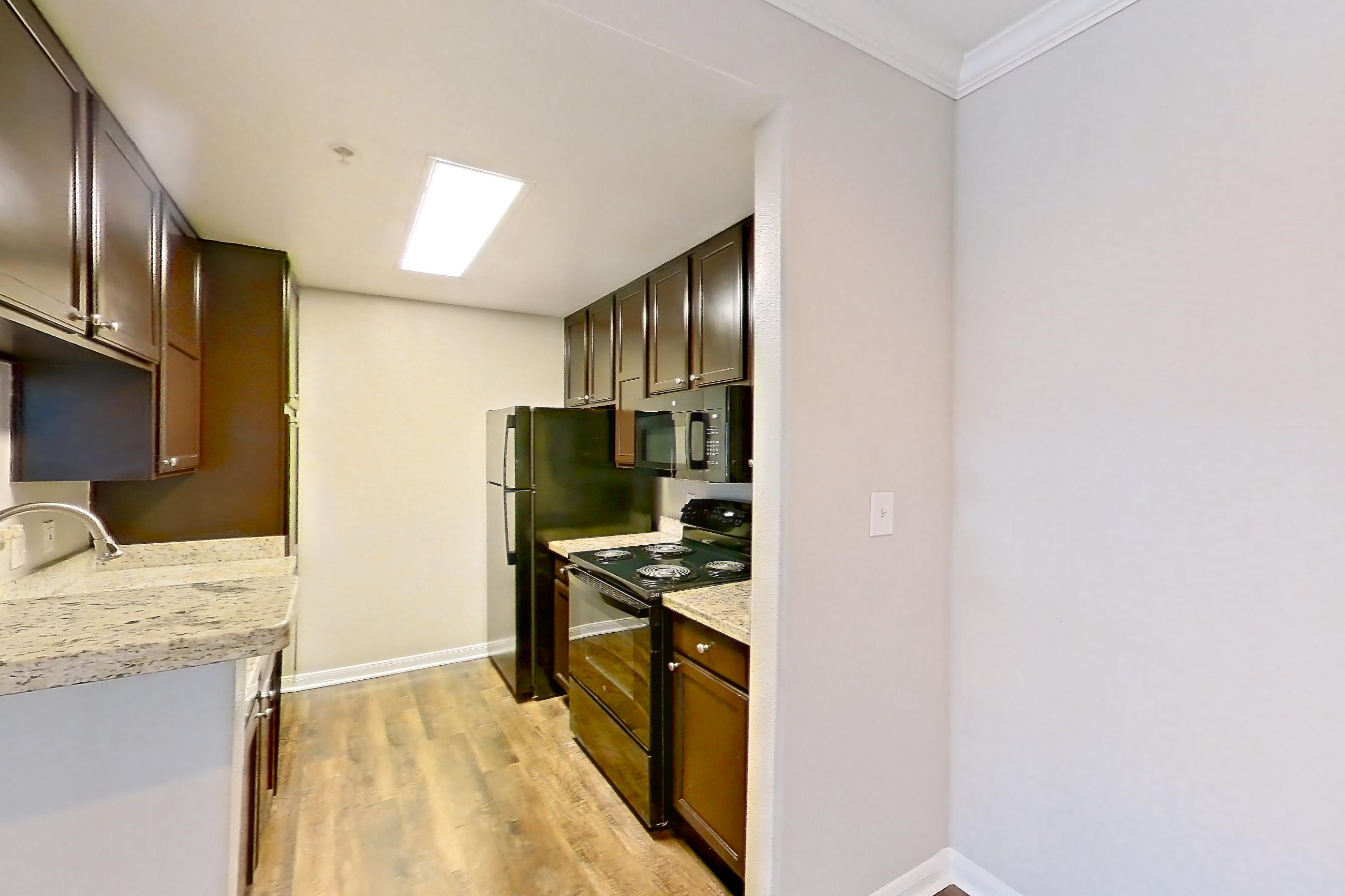 Dining room with black appliances, dark wood-finish flooring, electric range, fireplace, kitchen island, light countertops, light stone countertops, oven/range, refrigerator, and stainless steel appliances, Apartment 0636 at Marquis on Westheimer