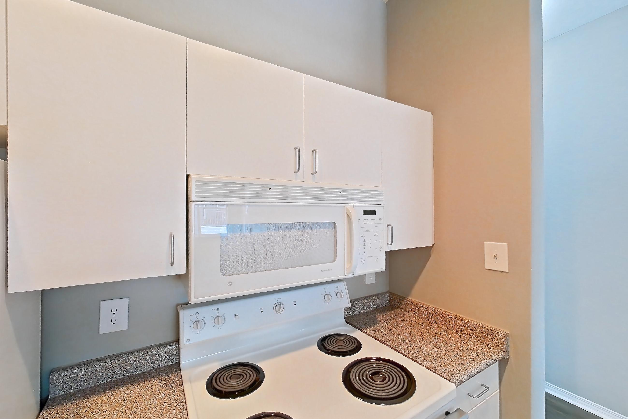 Kitchen with dishwasher, electric range, light countertops, light stone countertops, light wood-finish flooring, microwave, oven/range, refrigerator, and white appliances, Apartment 01-01313 at Marquis on Gaston