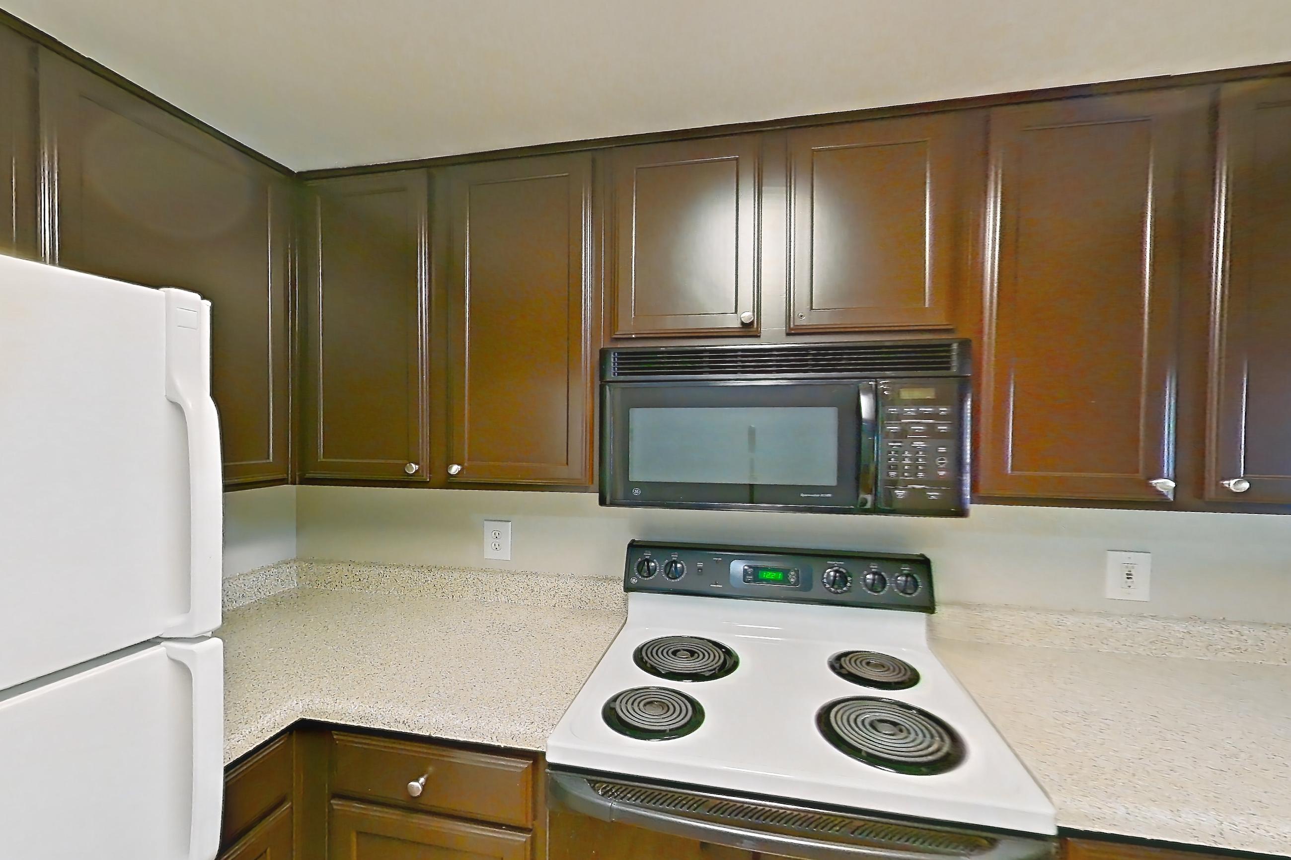 Kitchen with black appliances, electric range, light countertops, light stone countertops, light wood-finish flooring, microwave, oven/range, refrigerator, white appliances, and wood-finish flooring, Apartment 0732 at Marquis on Westheimer