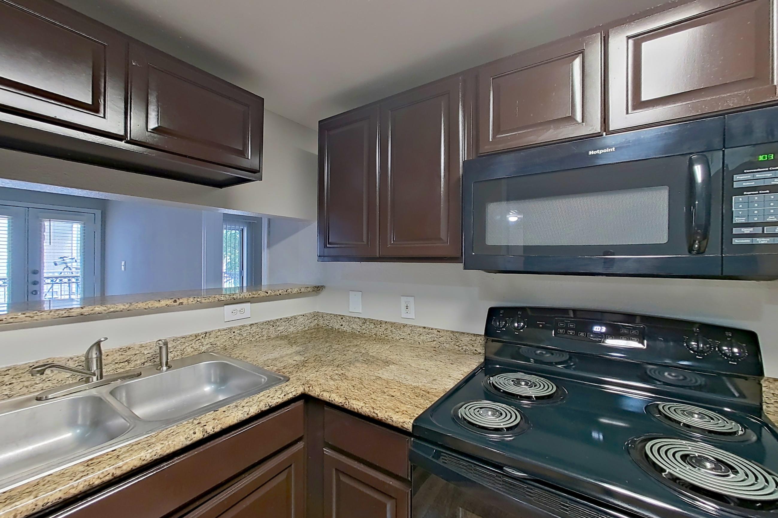 Kitchen with black appliances, dishwasher, electric range, light countertops, light stone countertops, light wood-finish flooring, microwave, oven/range, and refrigerator, Apartment 0821 at Marquis on Westheimer