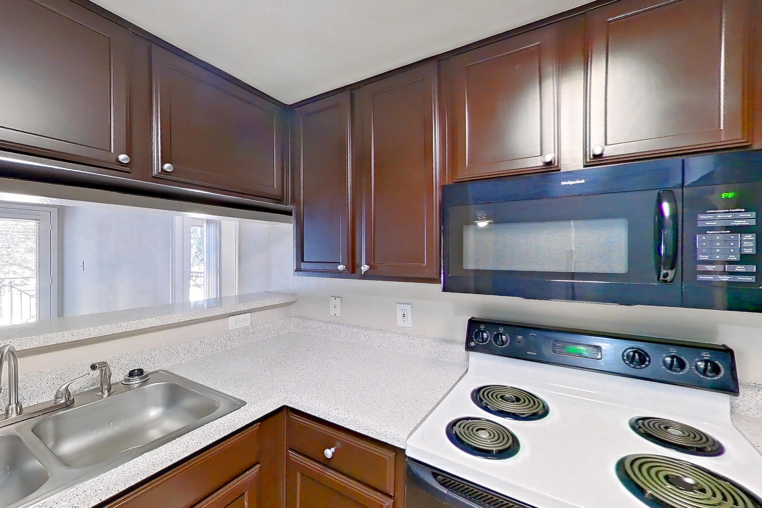 Kitchen with black appliances, dishwasher, electric range, light countertops, light stone countertops, light wood-finish flooring, microwave, oven/range, and white appliances, Apartment 0923 at Marquis on Westheimer