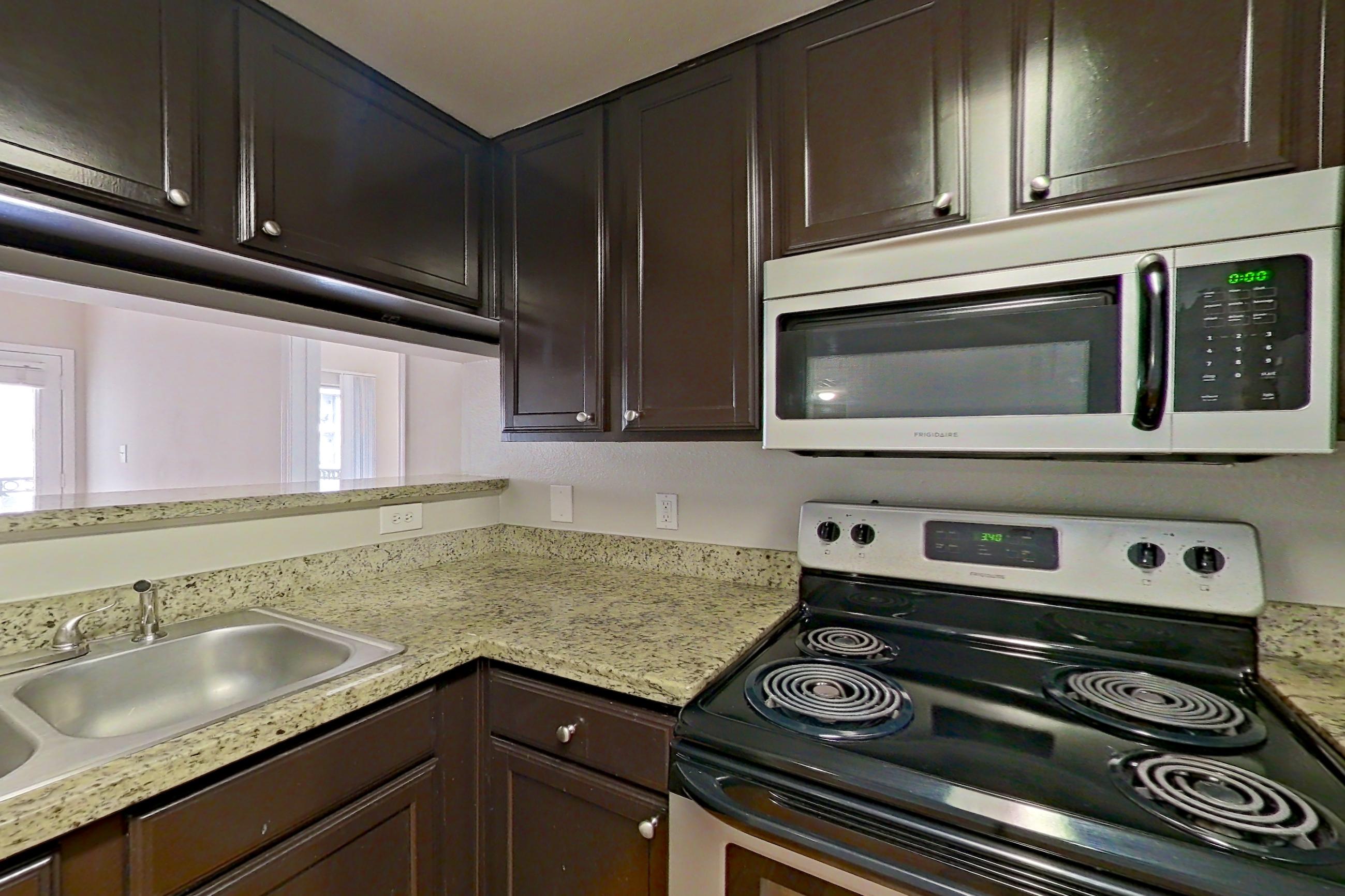 Kitchen with black appliances, dishwasher, electric range, light stone countertops, light wood-finish flooring, microwave, oven/range, and stainless steel appliances, Apartment 0927 at Marquis on Westheimer