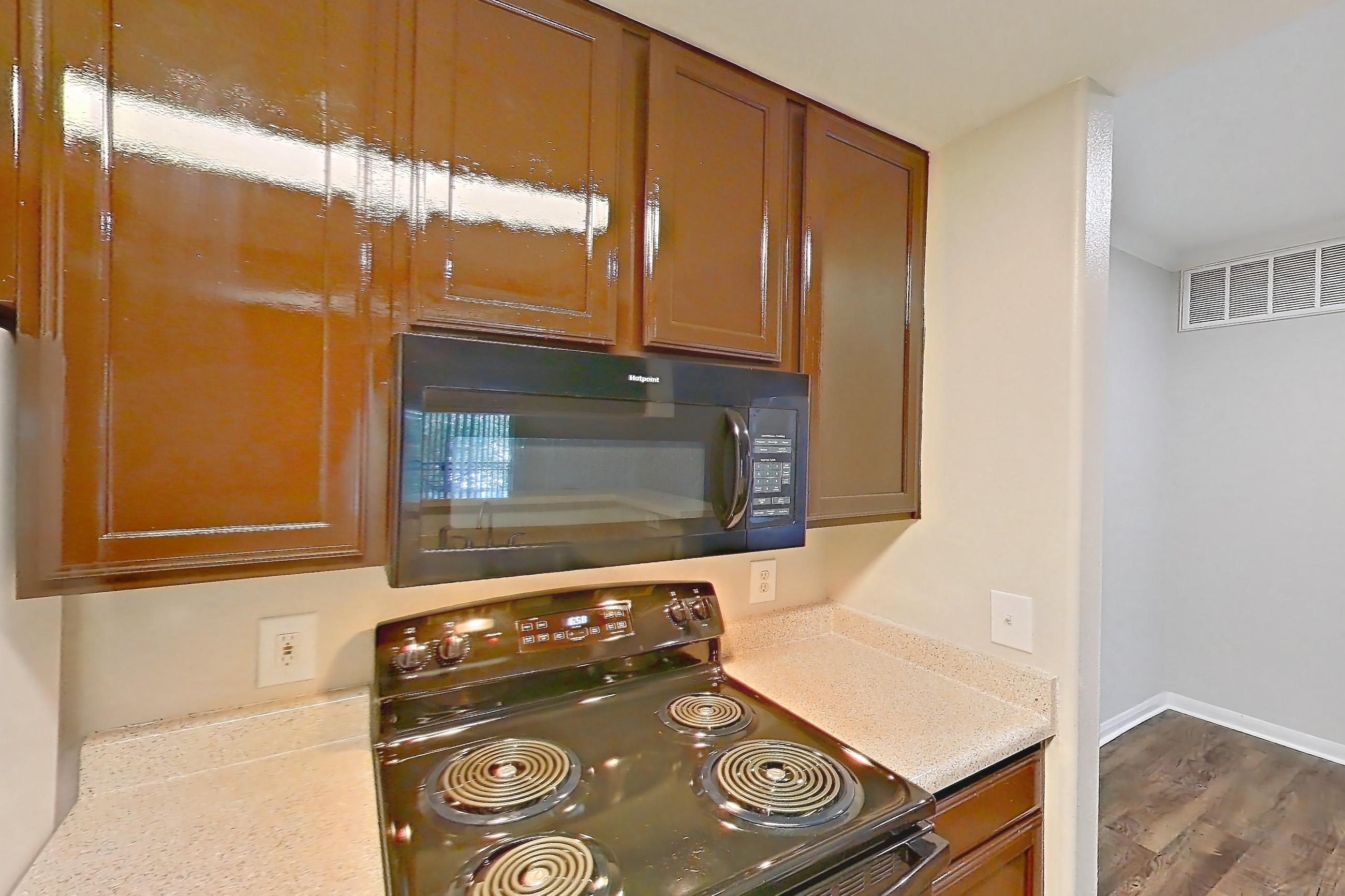 Kitchen with black appliances, dishwasher, electric range, light countertops, light stone countertops, light wood-finish flooring, microwave, oven/range, refrigerator, and white appliances, Apartment 0934 at Marquis on Westheimer