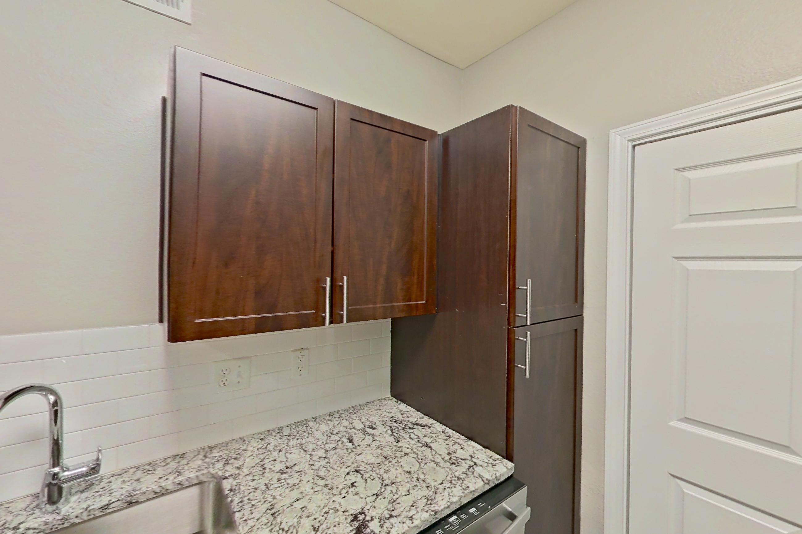 Kitchen with dishwasher, electric range, finished basement, light stone countertops, light wood-finish flooring, microwave, oven/range, and stainless steel appliances, Apartment 05-00512 at Marquis on Gaston