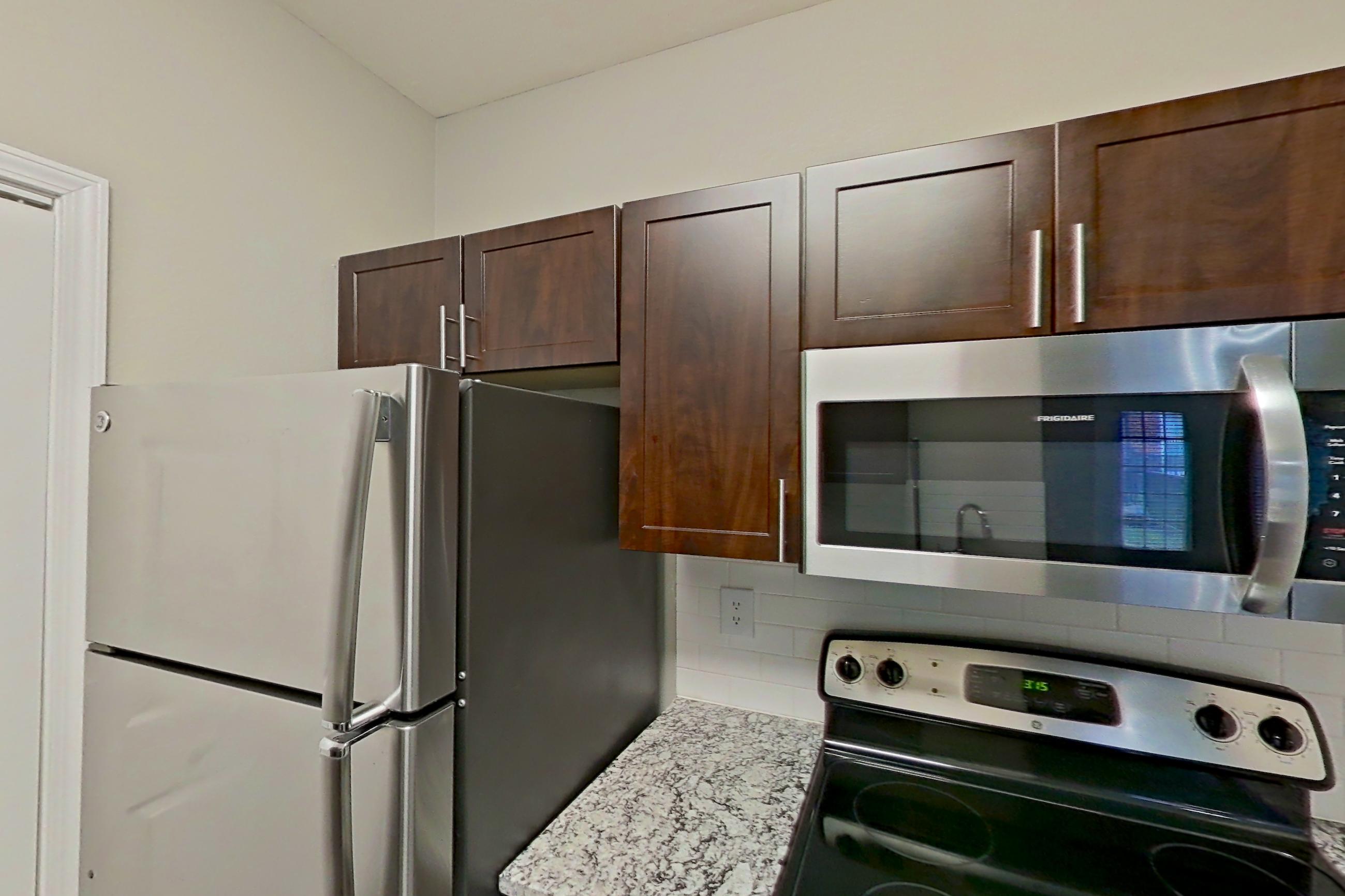 Kitchen with dishwasher, electric range, finished basement, light stone countertops, light wood-finish flooring, microwave, oven/range, and stainless steel appliances, Apartment 05-00512 at Marquis on Gaston