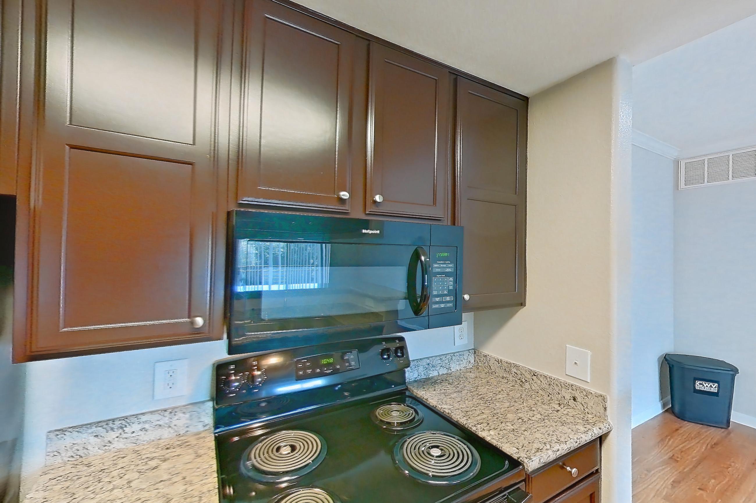 Kitchen with black appliances, dishwasher, electric range, light stone countertops, light wood-finish flooring, microwave, oven/range, refrigerator, and stainless steel appliances, Apartment 1138 at Marquis on Westheimer