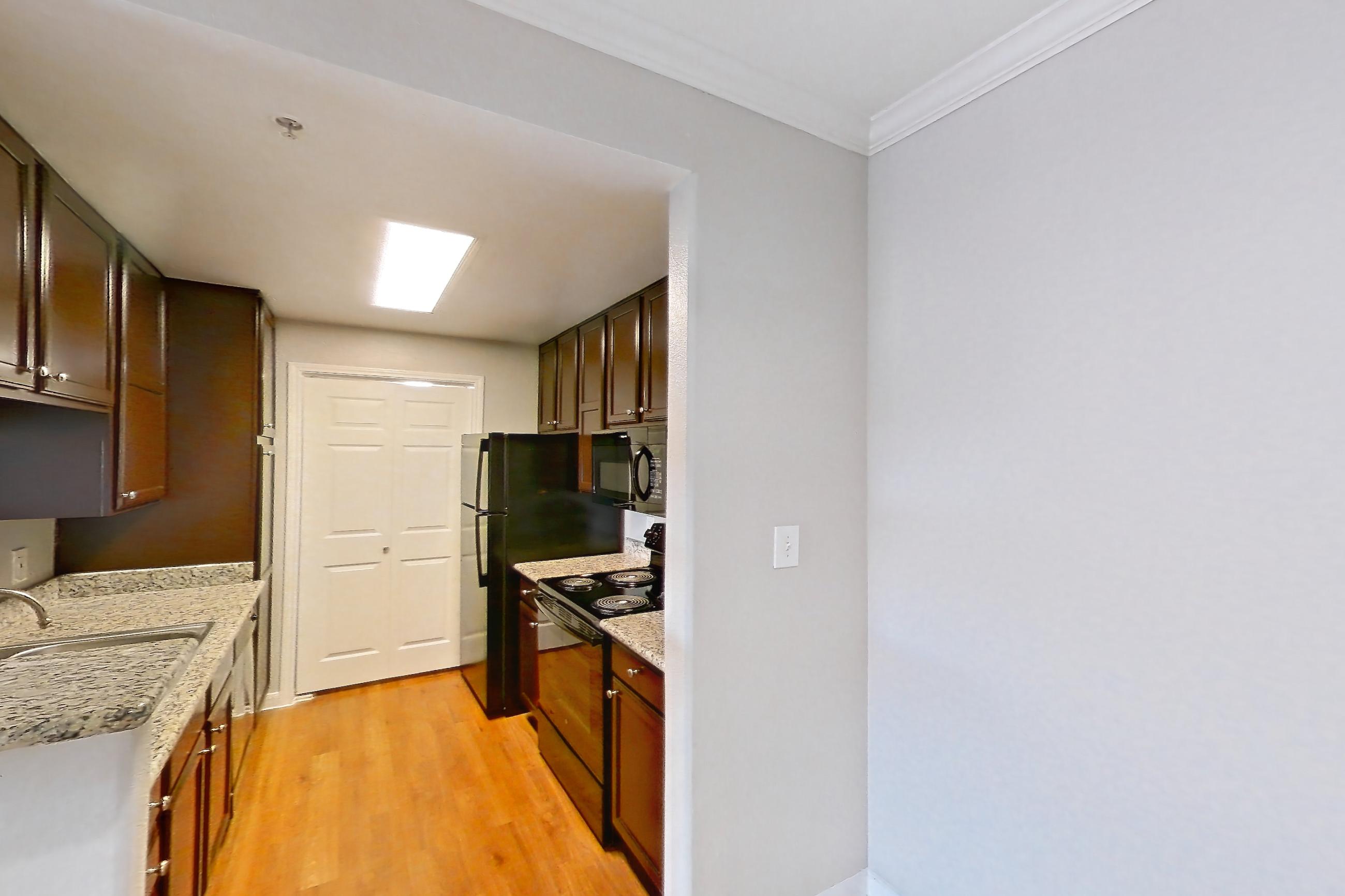 Living space with black appliances, electric range, light stone countertops, light wood-finish flooring, microwave, and oven/range, Apartment 1138 at Marquis on Westheimer