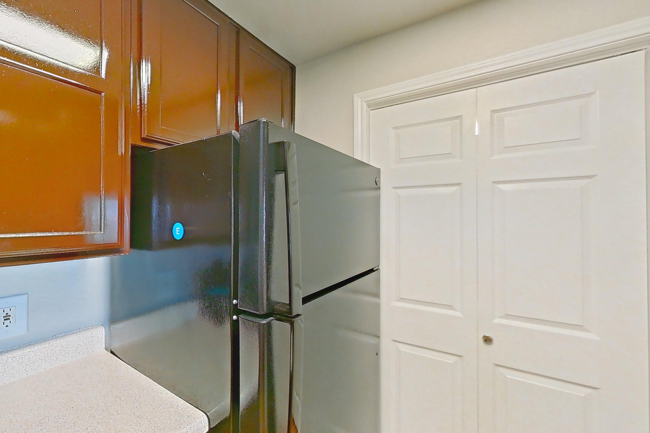 Kitchen with black appliances, dishwasher, electric range, light countertops, light stone countertops, light wood-finish flooring, oven/range, range hood, refrigerator, stainless steel appliances, white appliances, and wood-finish flooring, Apartment 1325 at Marquis on Westheimer