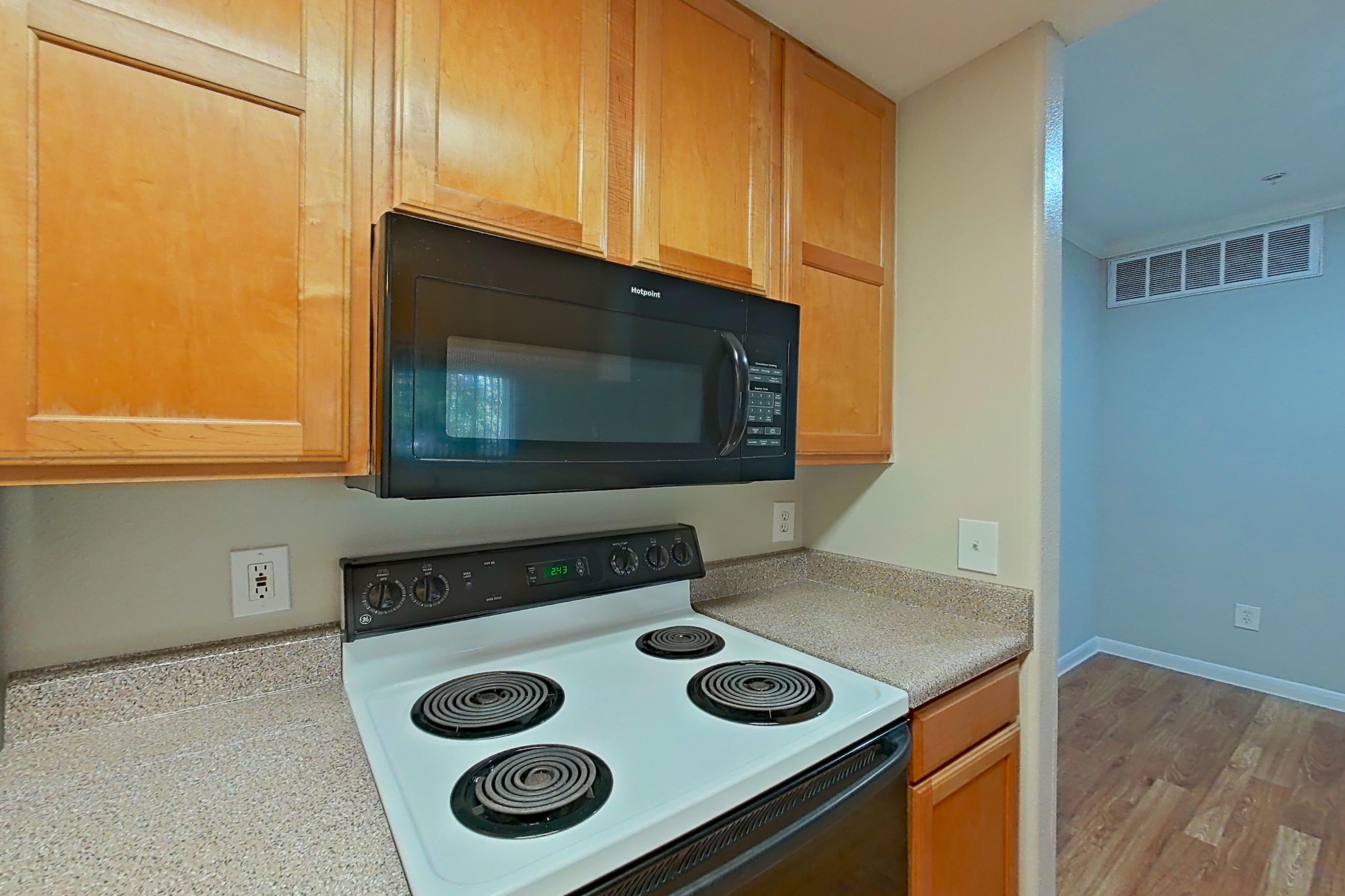 Kitchen with black appliances, dishwasher, electric range, light countertops, light wood-finish flooring, microwave, refrigerator, and white appliances, Apartment 1334 at Marquis on Westheimer