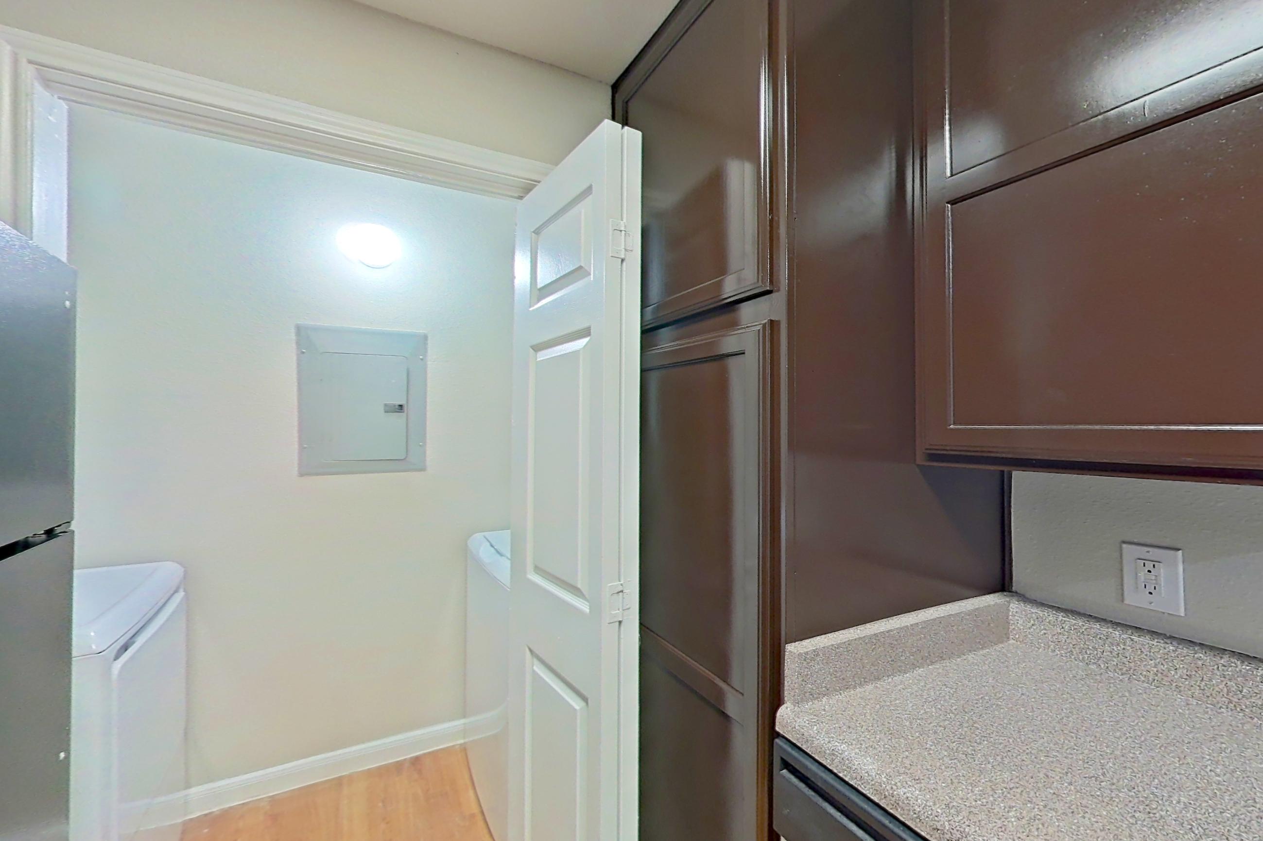 Kitchen with black appliances, dishwasher, electric range, in-unit laundry, light countertops, light wood-finish flooring, microwave, oven/range, refrigerator, and white appliances, Apartment 1411 at Marquis on Westheimer