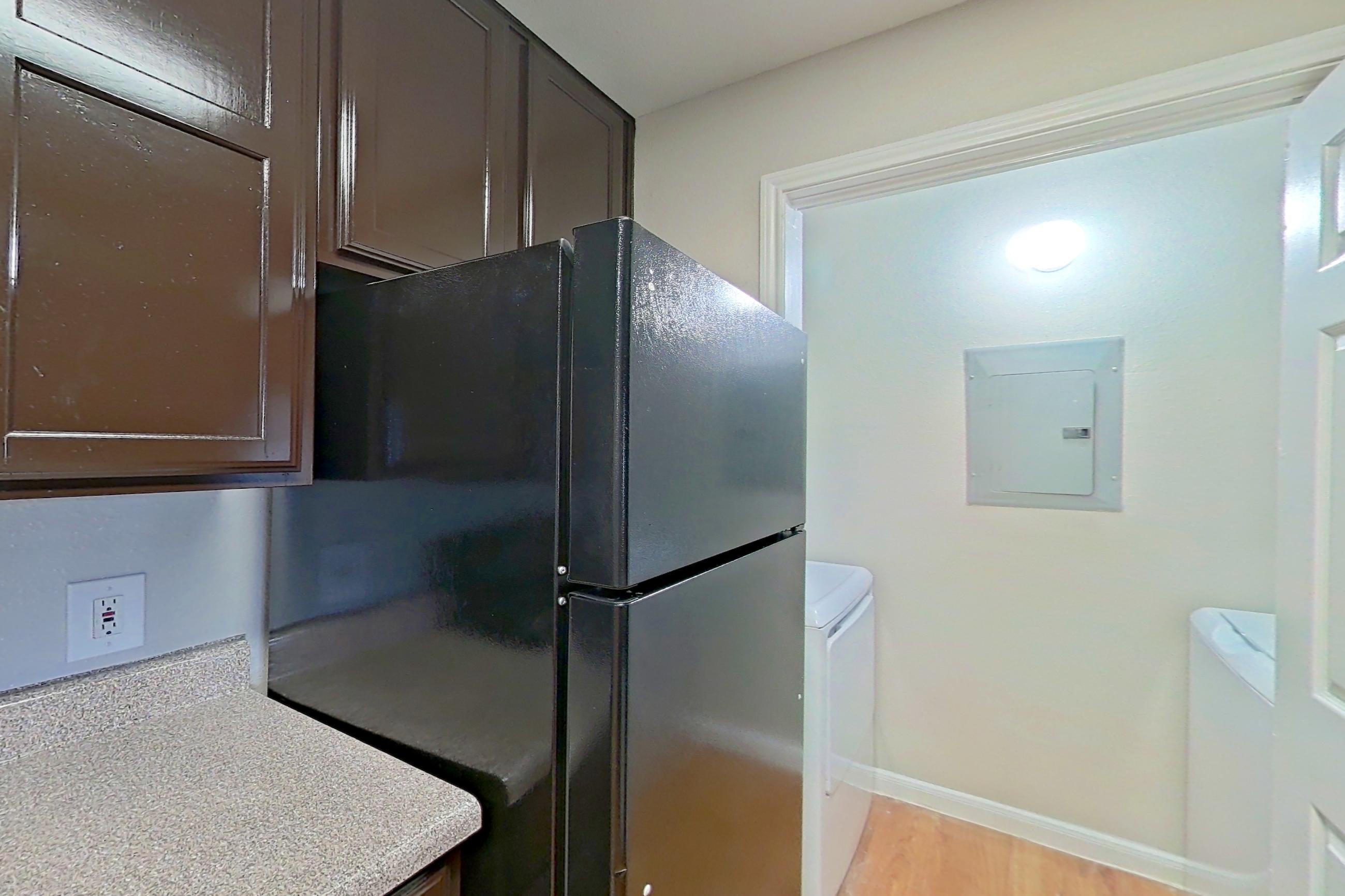 Kitchen with black appliances, dishwasher, electric range, in-unit laundry, light countertops, light wood-finish flooring, microwave, oven/range, refrigerator, and white appliances, Apartment 1411 at Marquis on Westheimer