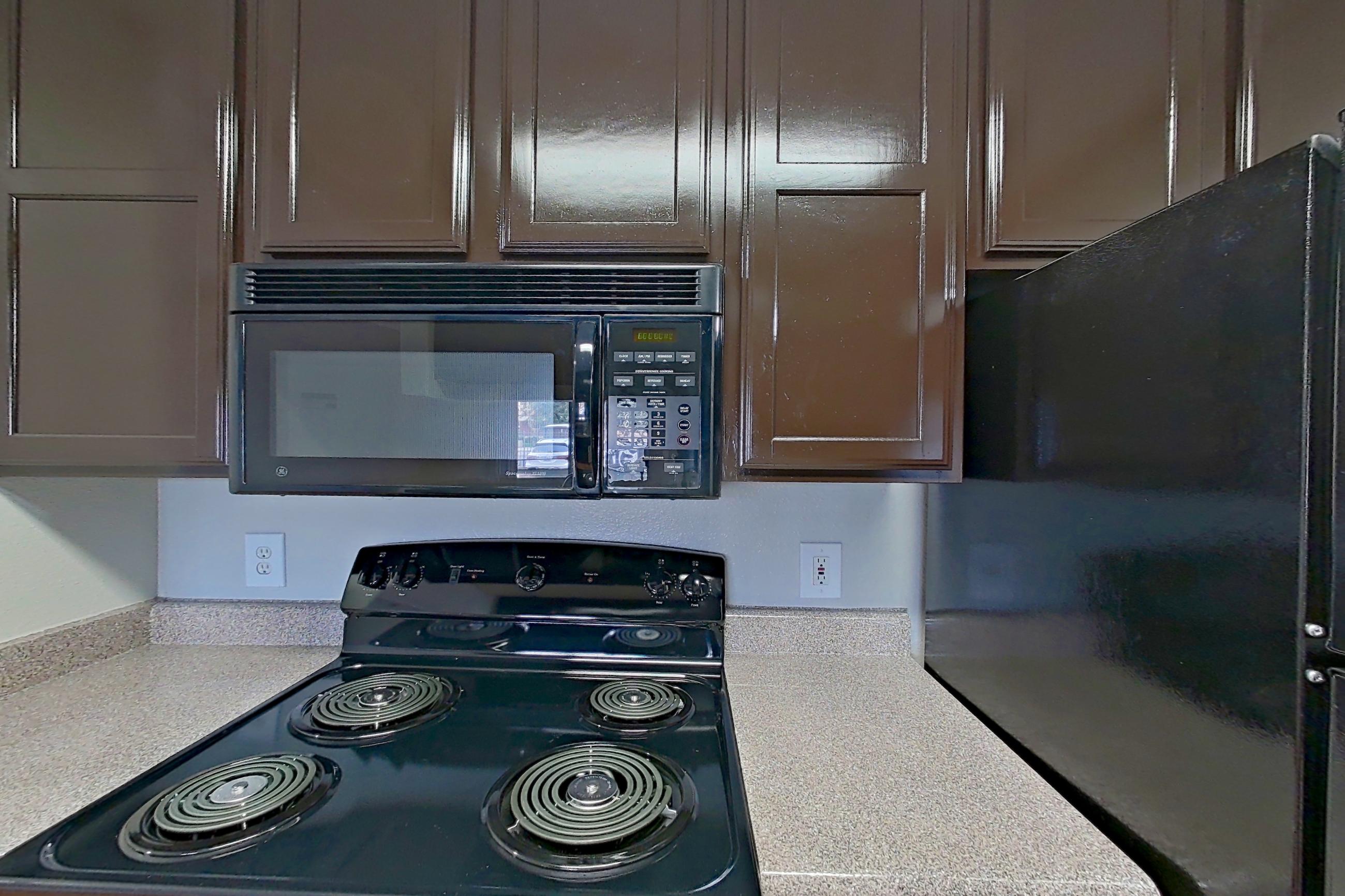 Kitchen with black appliances, dishwasher, electric range, in-unit laundry, light countertops, light wood-finish flooring, microwave, oven/range, refrigerator, and white appliances, Apartment 1411 at Marquis on Westheimer