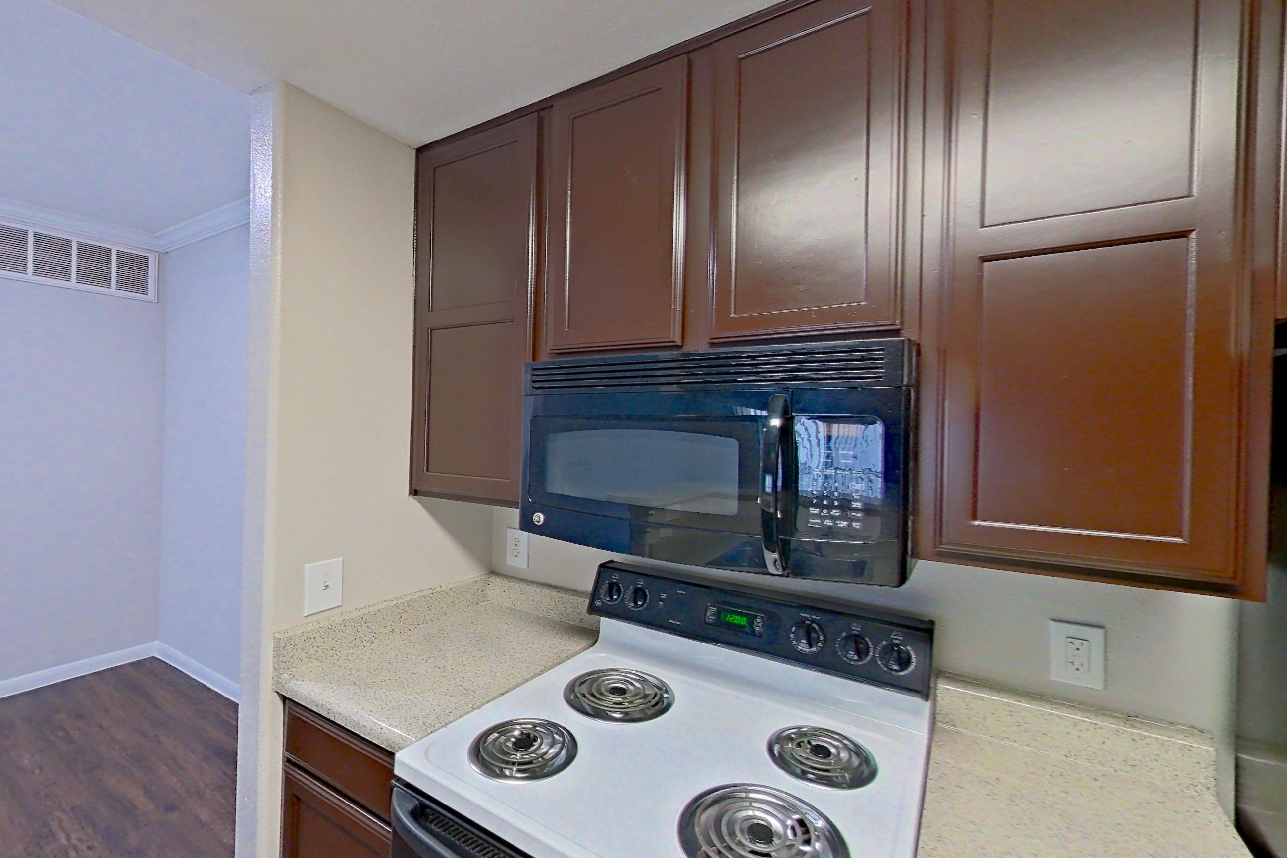 Kitchen with black appliances, dark wood-finish flooring, dishwasher, electric range, light countertops, light stone countertops, microwave, oven/range, refrigerator, and white appliances, Apartment 1435 at Marquis on Westheimer