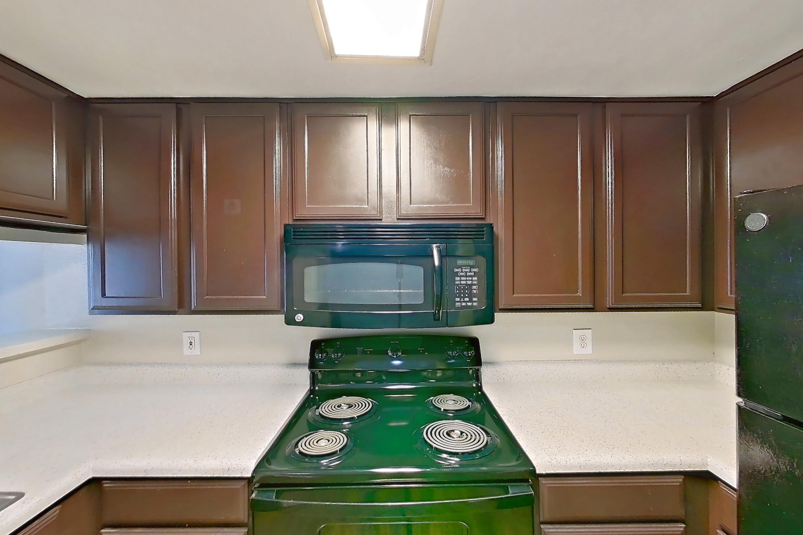 Kitchen with black appliances, dishwasher, electric range, glass shower door, light countertops, light stone countertops, light wood-finish flooring, microwave, oven/range, refrigerator, stall shower, walk-in shower, and white appliances, Apartment 1437 at Marquis on Westheimer