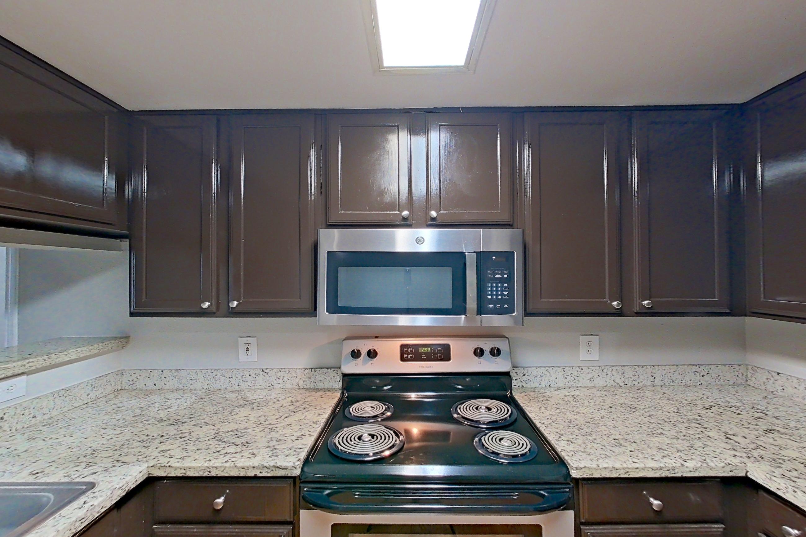 Kitchen with electric range, light stone countertops, light wood-finish flooring, microwave, oven/range, refrigerator, and stainless steel appliances, Apartment 1427 at Marquis on Westheimer