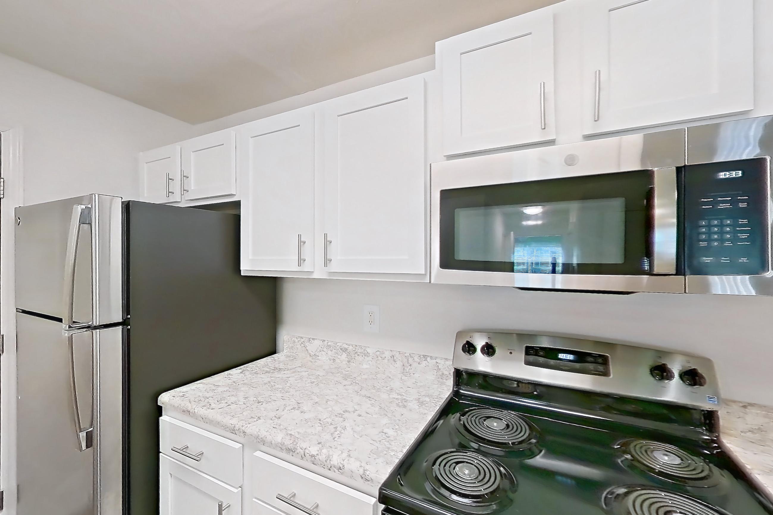 Kitchen with dark wood-finish flooring, electric range, light countertops, microwave, oven/range, refrigerator, and stainless steel appliances, Apartment 09-1016 at Marquis on Cary Parkway