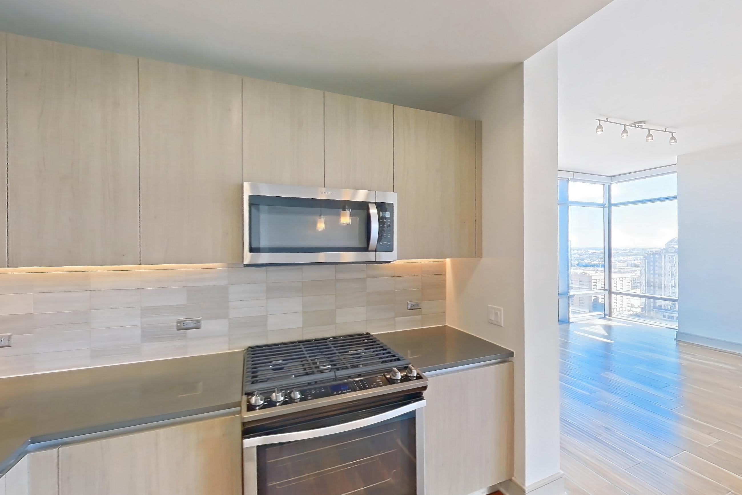 Kitchen with dark countertops, gas range, light countertops, light wood-finish flooring, oven/range, refrigerator, stainless steel appliances, and water & ice dispenser, Apartment 2810 at Aris Market Square