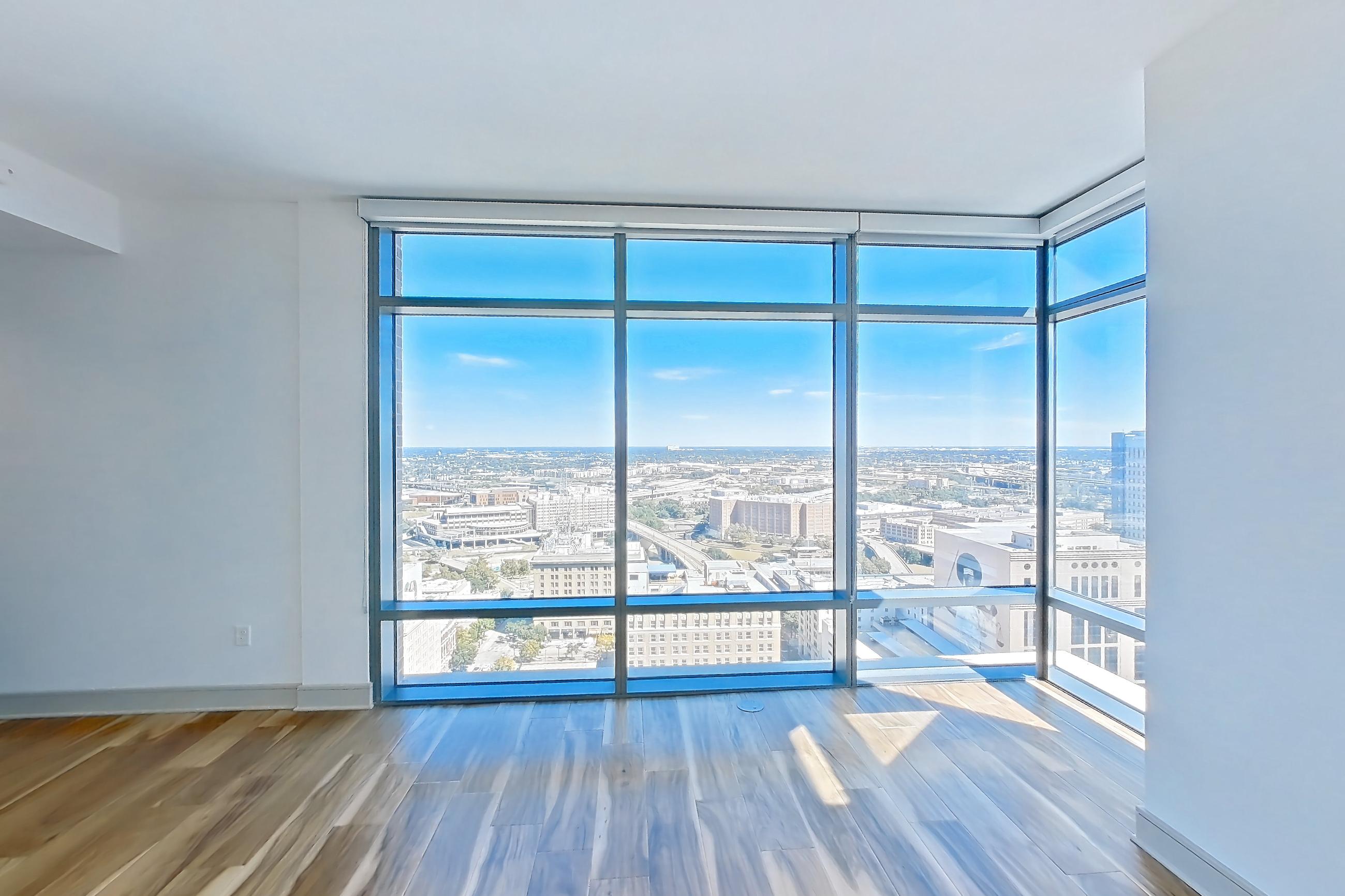Living room with city view, dark countertops, dishwasher, light wood-finish flooring, oven/range, refrigerator, stainless steel appliances, and water & ice dispenser, Apartment 2810 at Aris Market Square