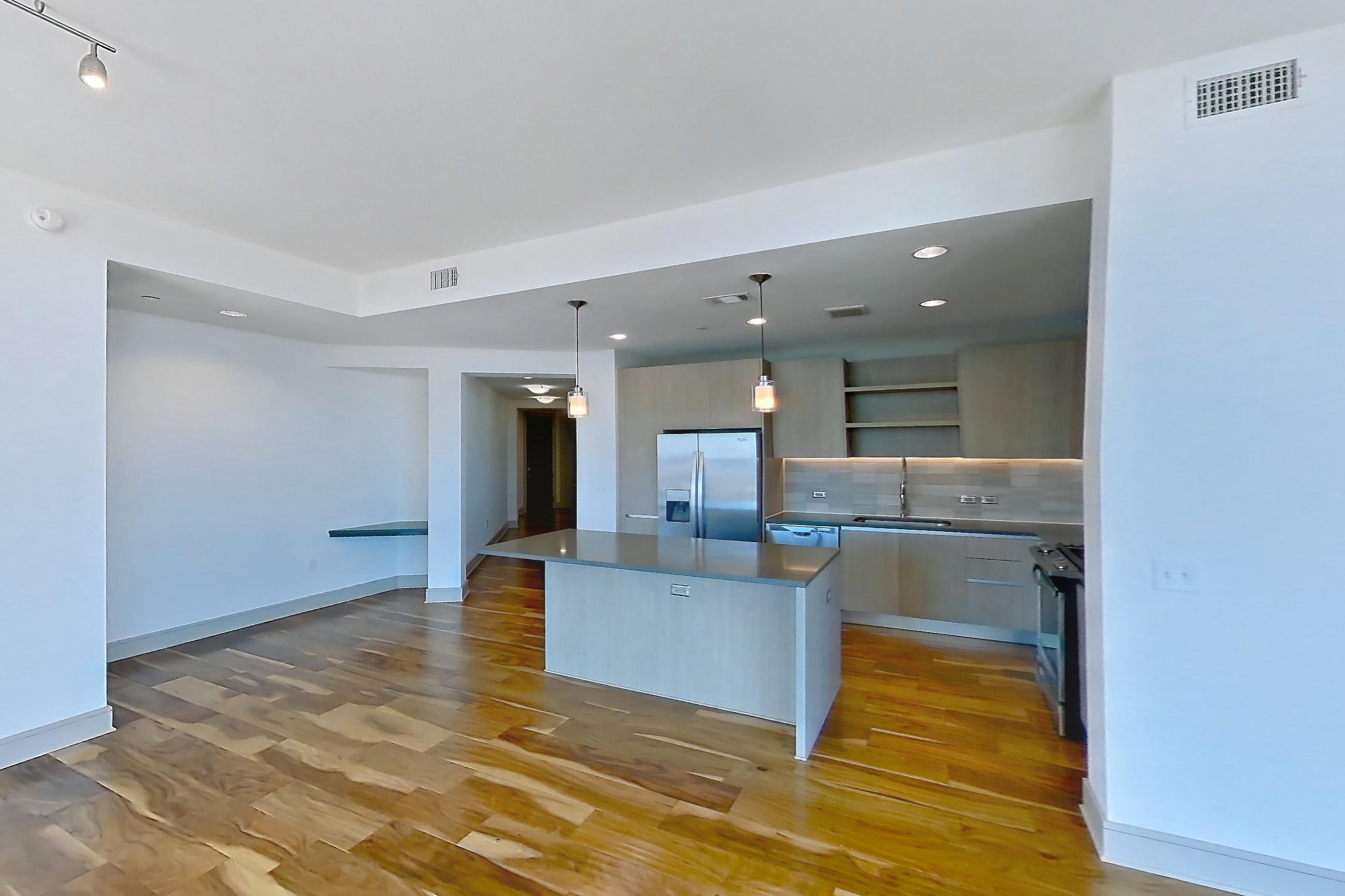 Living room with city view, dark countertops, dishwasher, light wood-finish flooring, oven/range, refrigerator, stainless steel appliances, and water & ice dispenser, Apartment 2810 at Aris Market Square