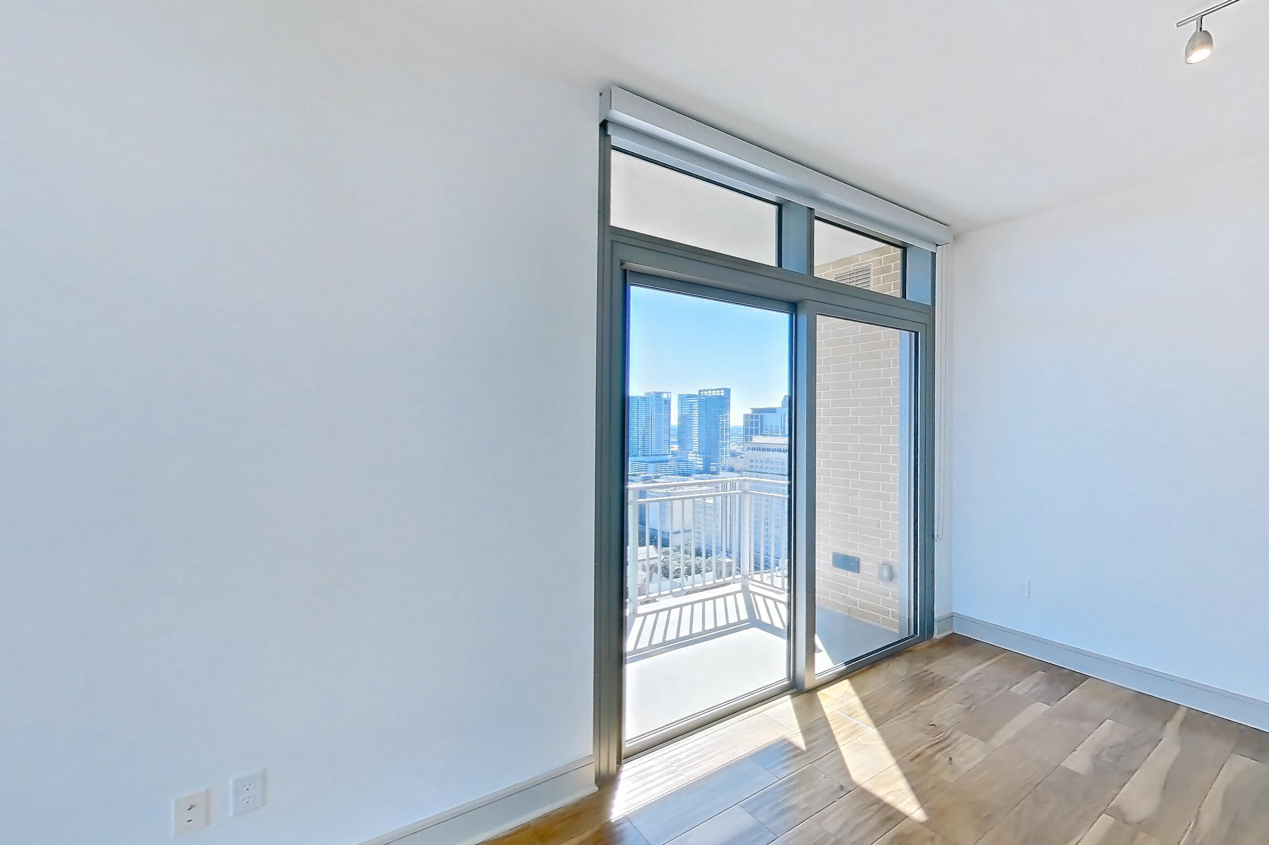 Living room with city view, dark countertops, dishwasher, light wood-finish flooring, oven/range, refrigerator, stainless steel appliances, and water & ice dispenser, Apartment 2810 at Aris Market Square