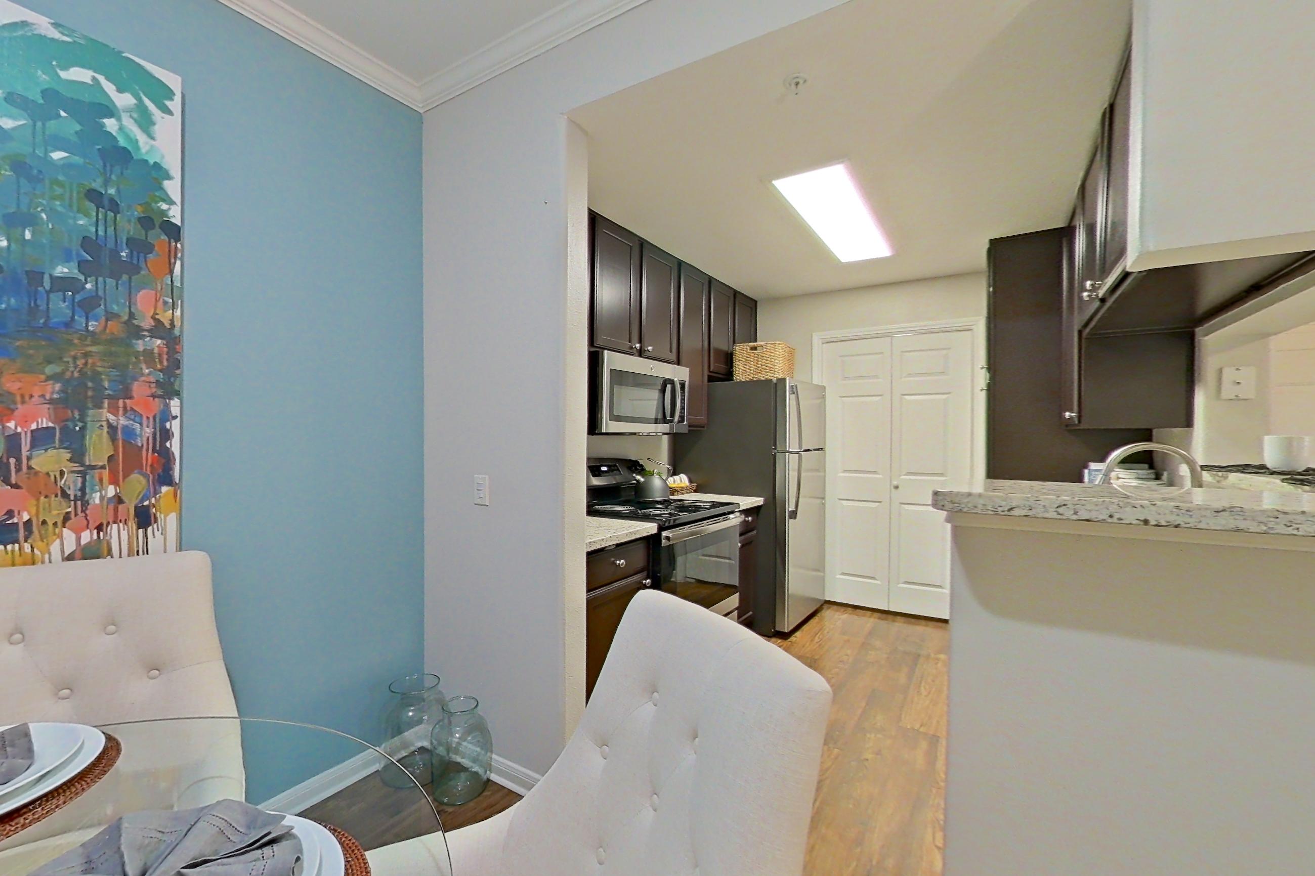 Dining room with light countertops, light stone countertops, refrigerator, stainless steel appliances, and wood-finish flooring, Apartment 0115 at Marquis on Westheimer