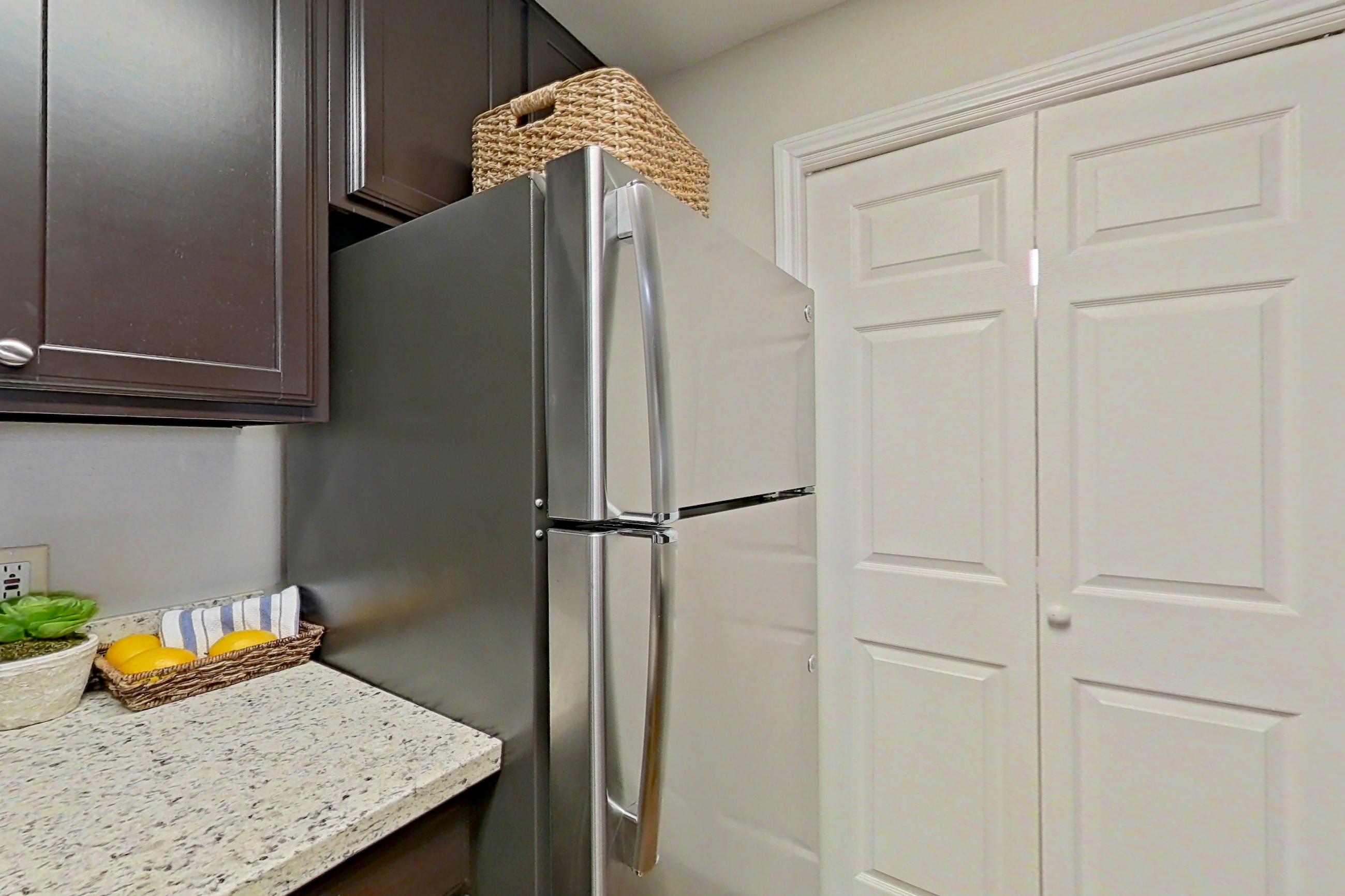 Kitchen with dishwasher, electric range, in-unit laundry, light stone countertops, light wood-finish flooring, refrigerator, and stainless steel appliances, Apartment 0115 at Marquis on Westheimer