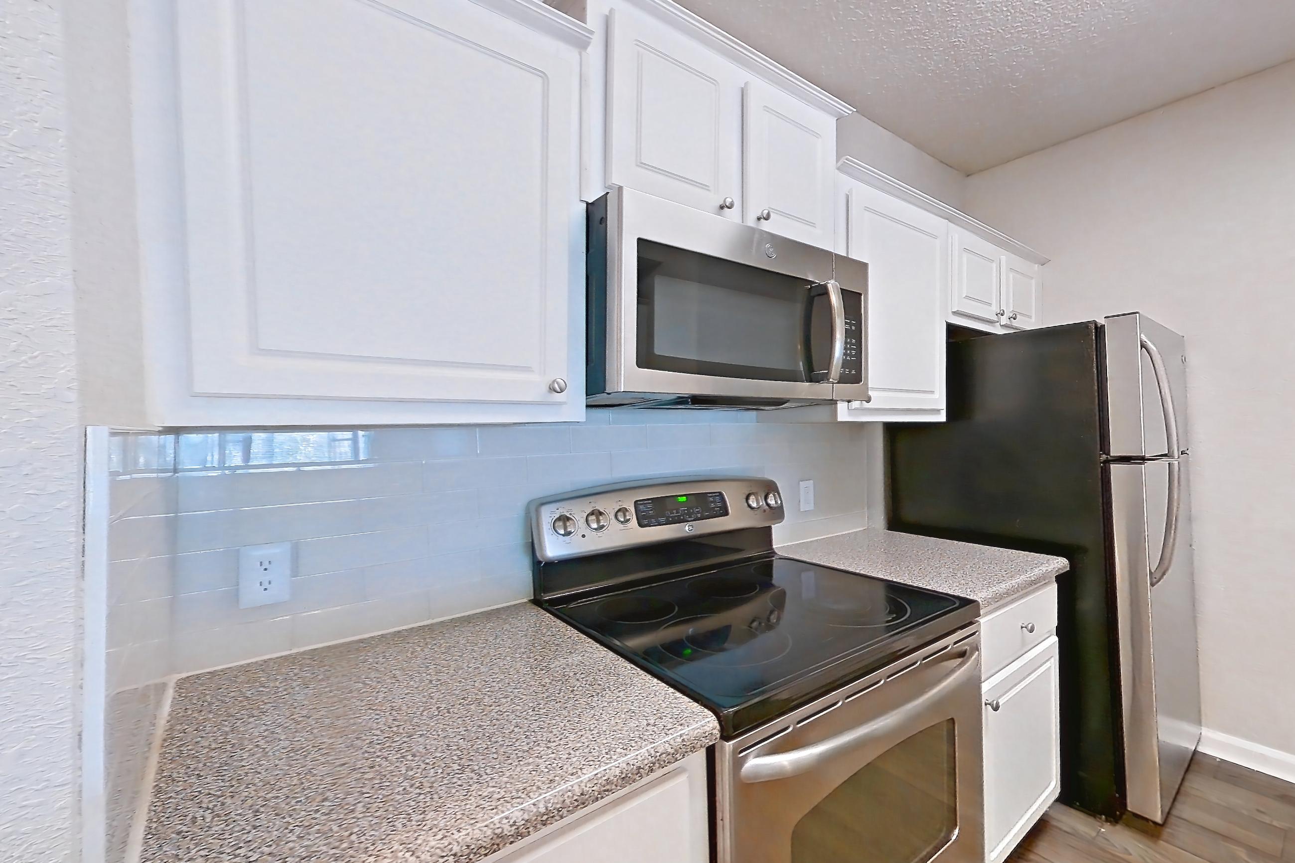 Kitchen with dishwasher, electric range, light countertops, light stone countertops, microwave, oven/range, refrigerator, and stainless steel appliances, Apartment 124 at Marquis Midtown West
