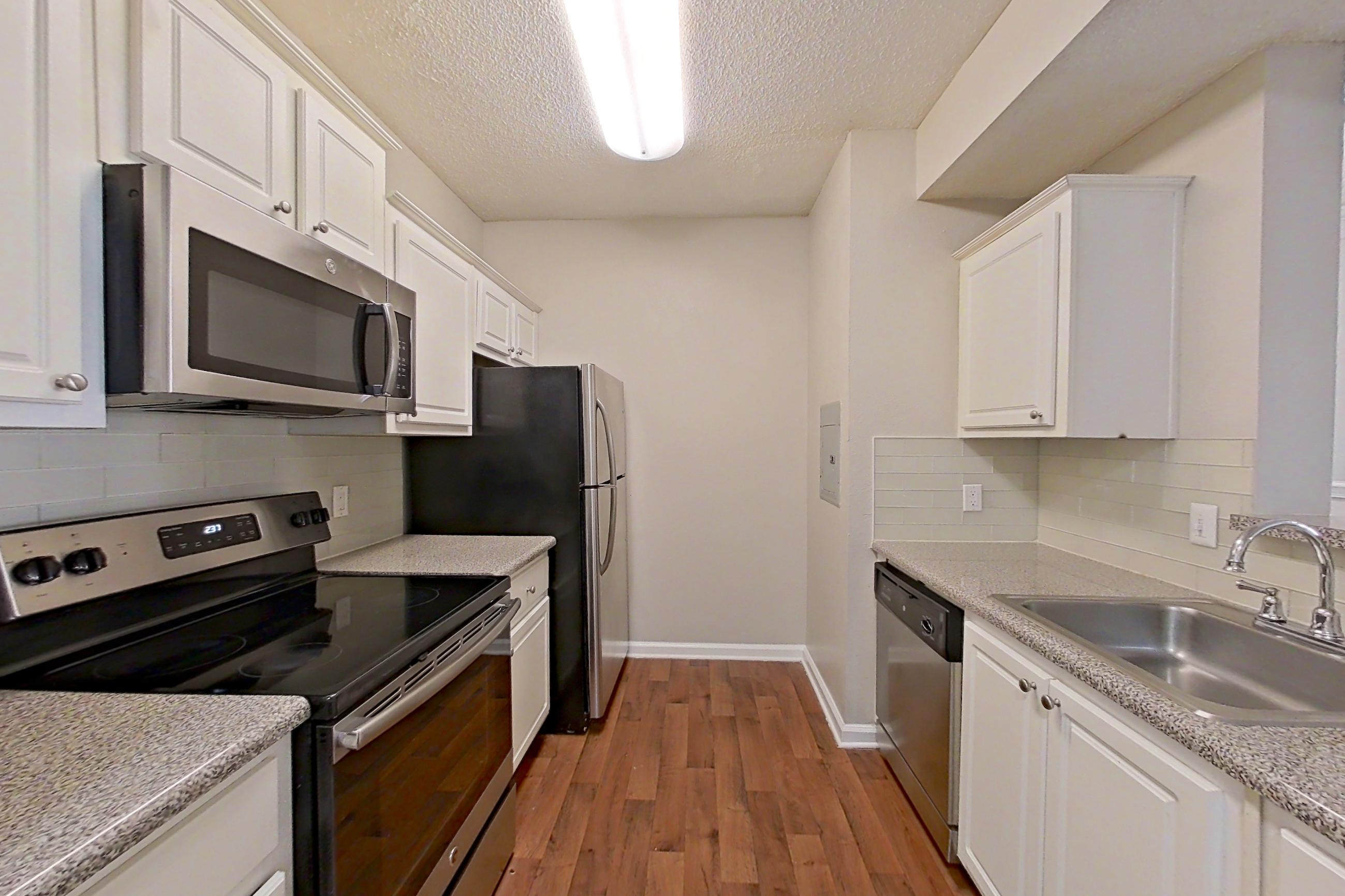 Kitchen with black appliances, dark wood-finish flooring, dishwasher, electric range, light countertops, light stone countertops, microwave, oven/range, refrigerator, and stainless steel appliances, Apartment 206 at Marquis Midtown West
