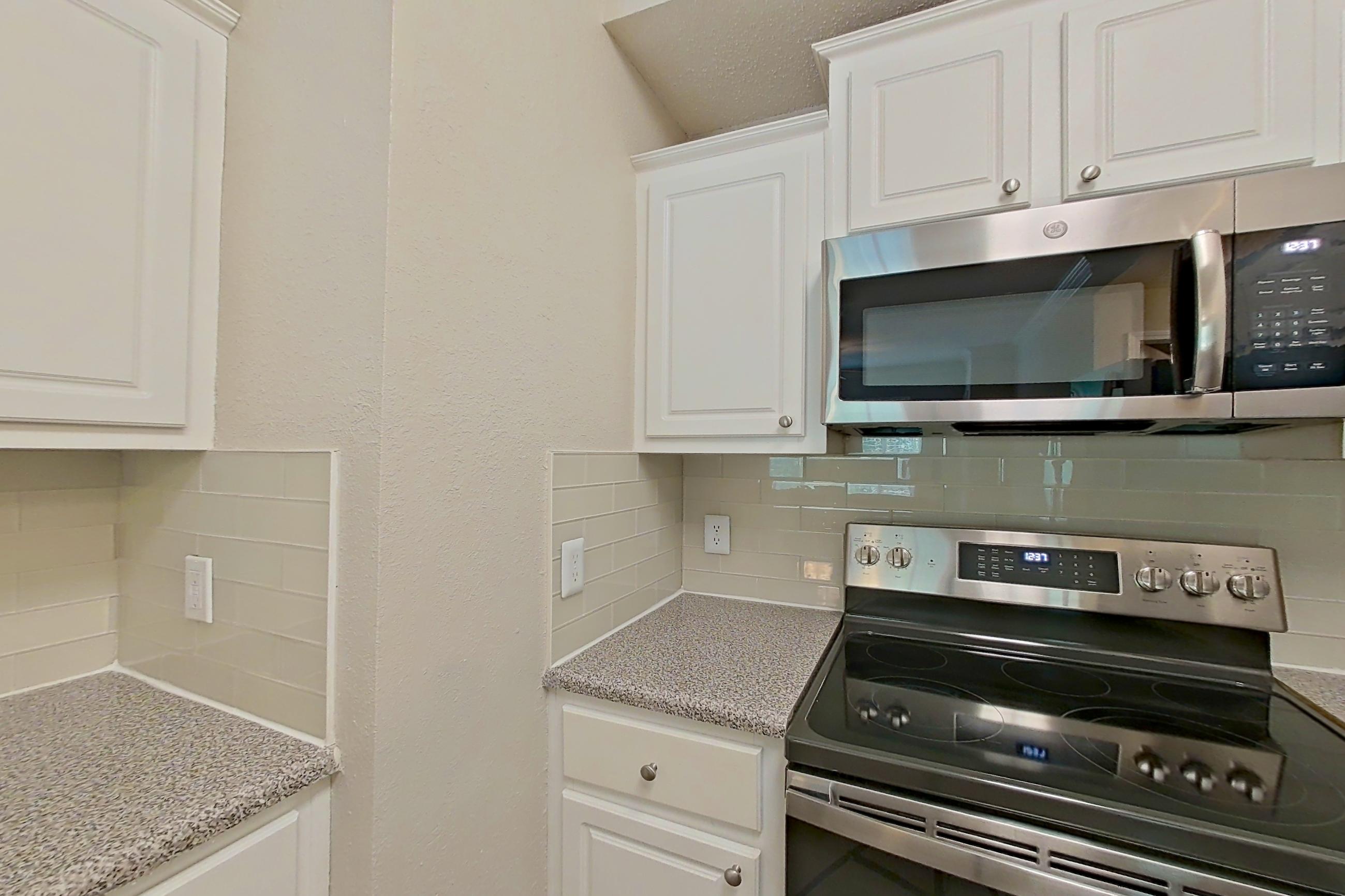 Kitchen with dark wood-finish flooring, dishwasher, electric range, light countertops, light stone countertops, microwave, oven/range, refrigerator, and stainless steel appliances, Apartment 434 at Marquis Midtown West