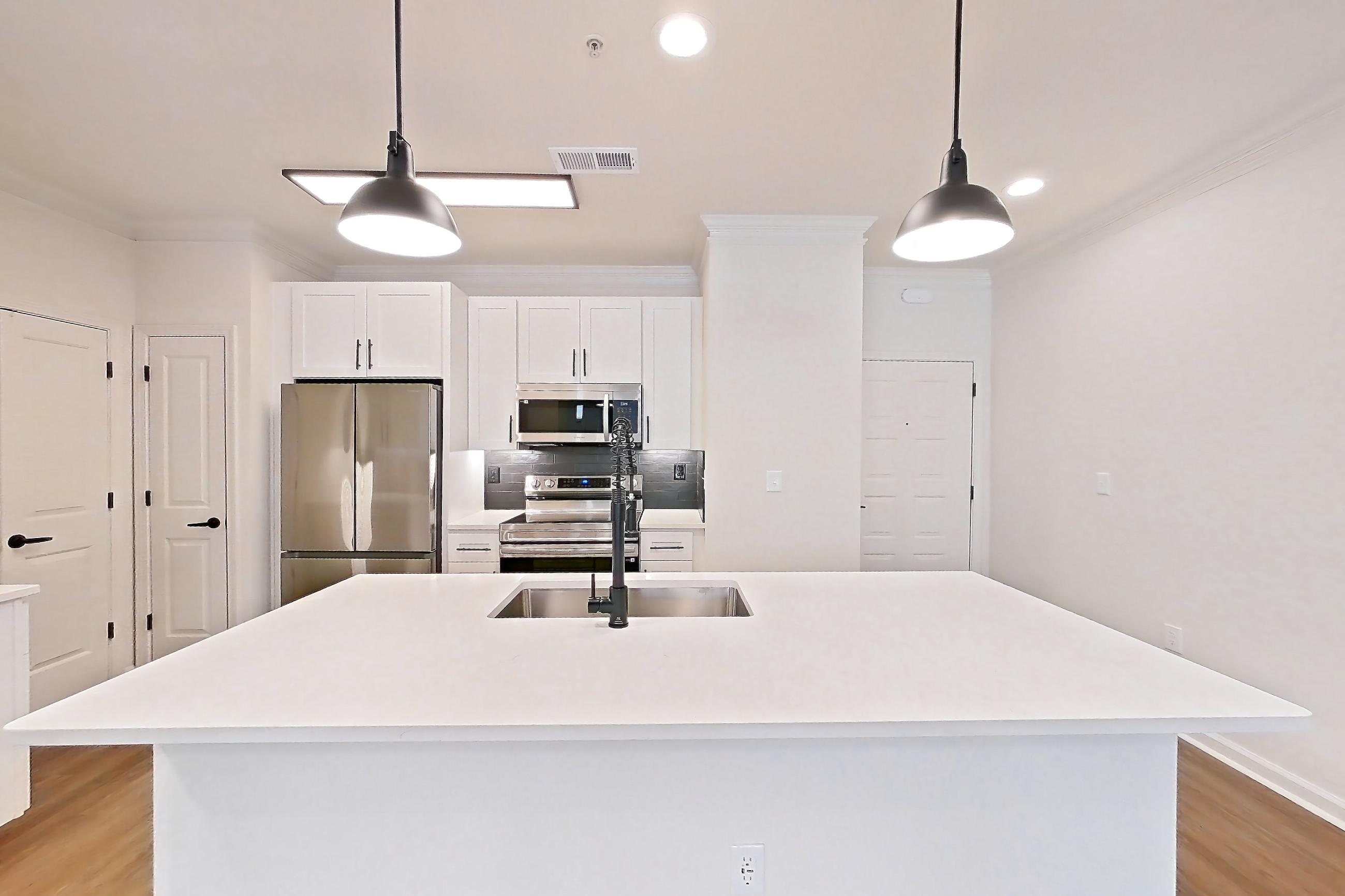 Dining room with electric range, kitchen island, light stone countertops, light wood-finish flooring, microwave, oven/range, refrigerator, and stainless steel appliances, Apartment 1110 at Cortland at Armour Yards
