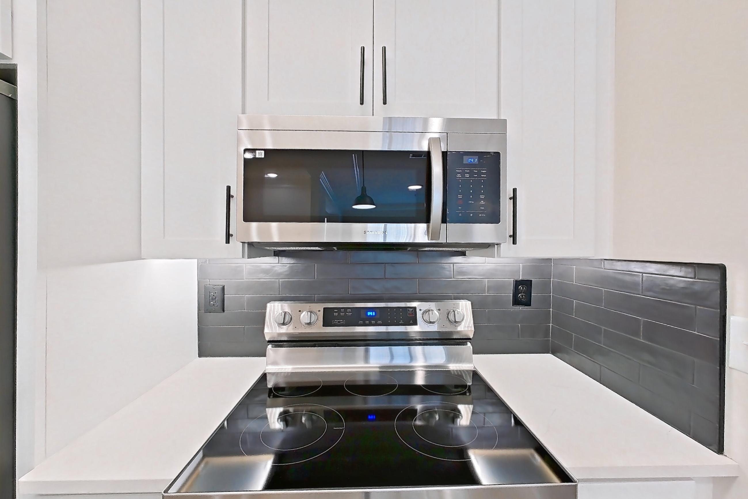 Kitchen with dishwasher, electric range, light countertops, light stone countertops, light wood-finish flooring, microwave, oven/range, refrigerator, and stainless steel appliances, Apartment 1110 at Cortland at Armour Yards