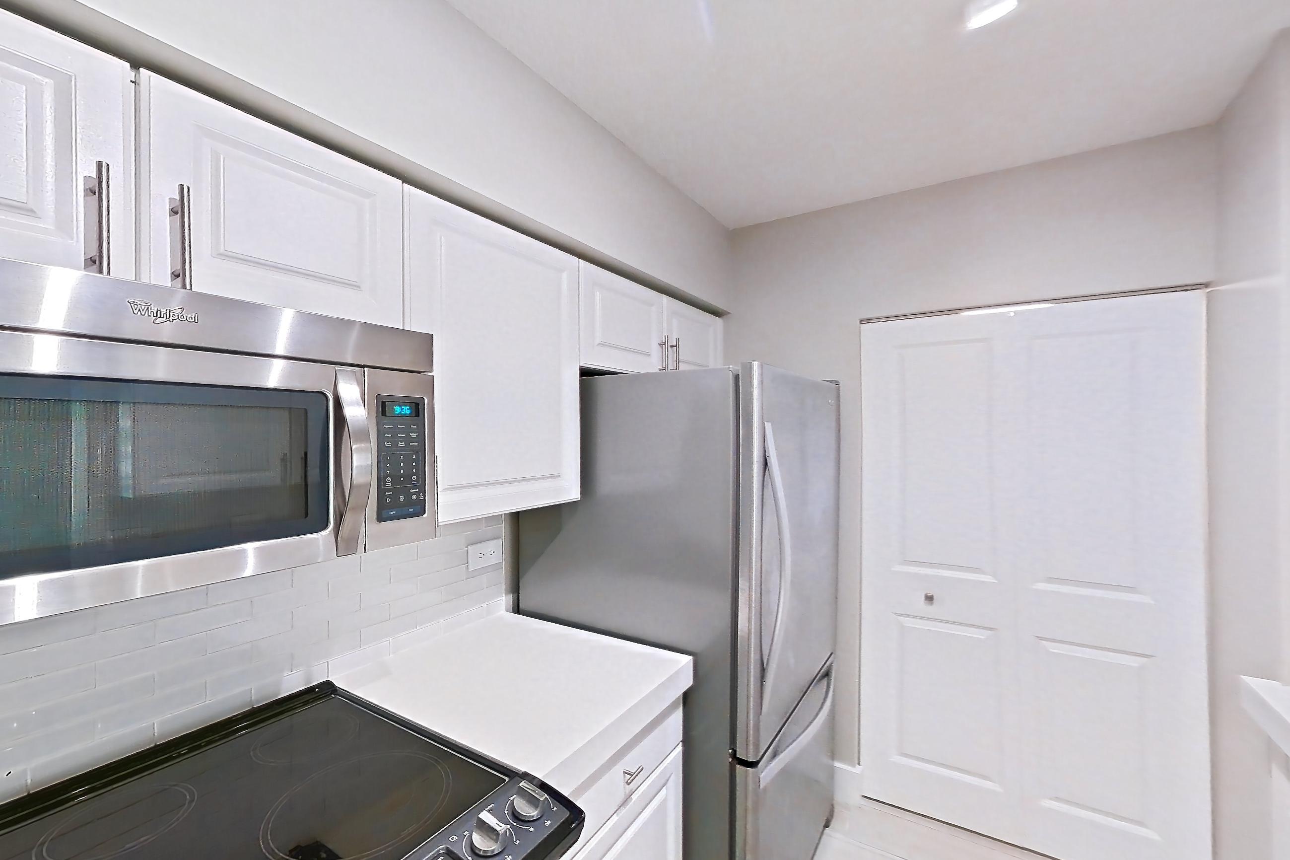 Kitchen with dishwasher, electric range, light countertops, light stone countertops, light tile flooring, light wood-finish flooring, oven/range, refrigerator, stainless steel appliances, and wood-look tile flooring, Apartment 0210 at Sunrise Harbor