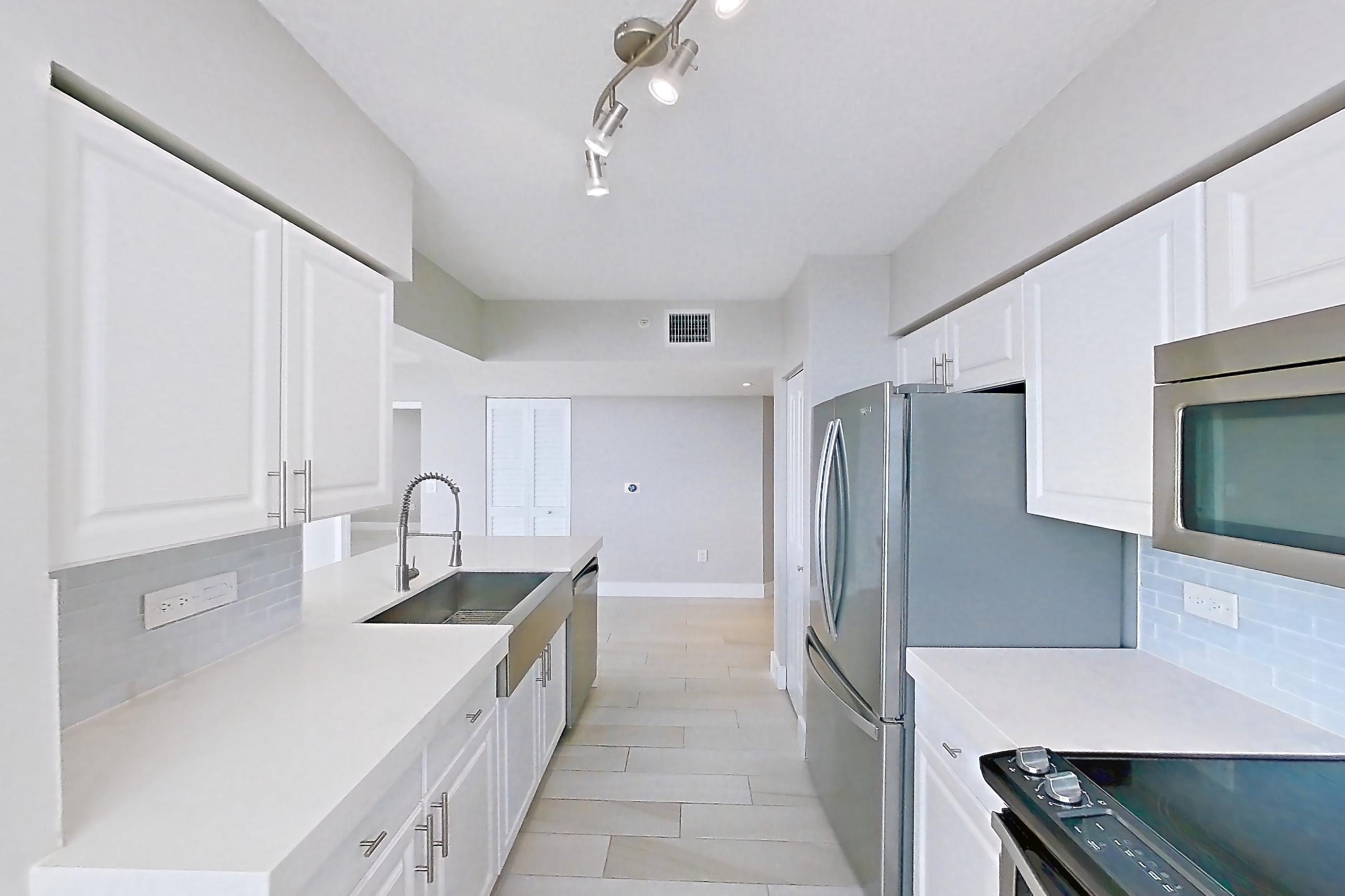 Kitchen window side with dishwasher, electric range, light countertops, light stone countertops, light wood-finish flooring, microwave, oven/range, refrigerator, and stainless steel appliances, Apartment 0808 at Sunrise Harbor