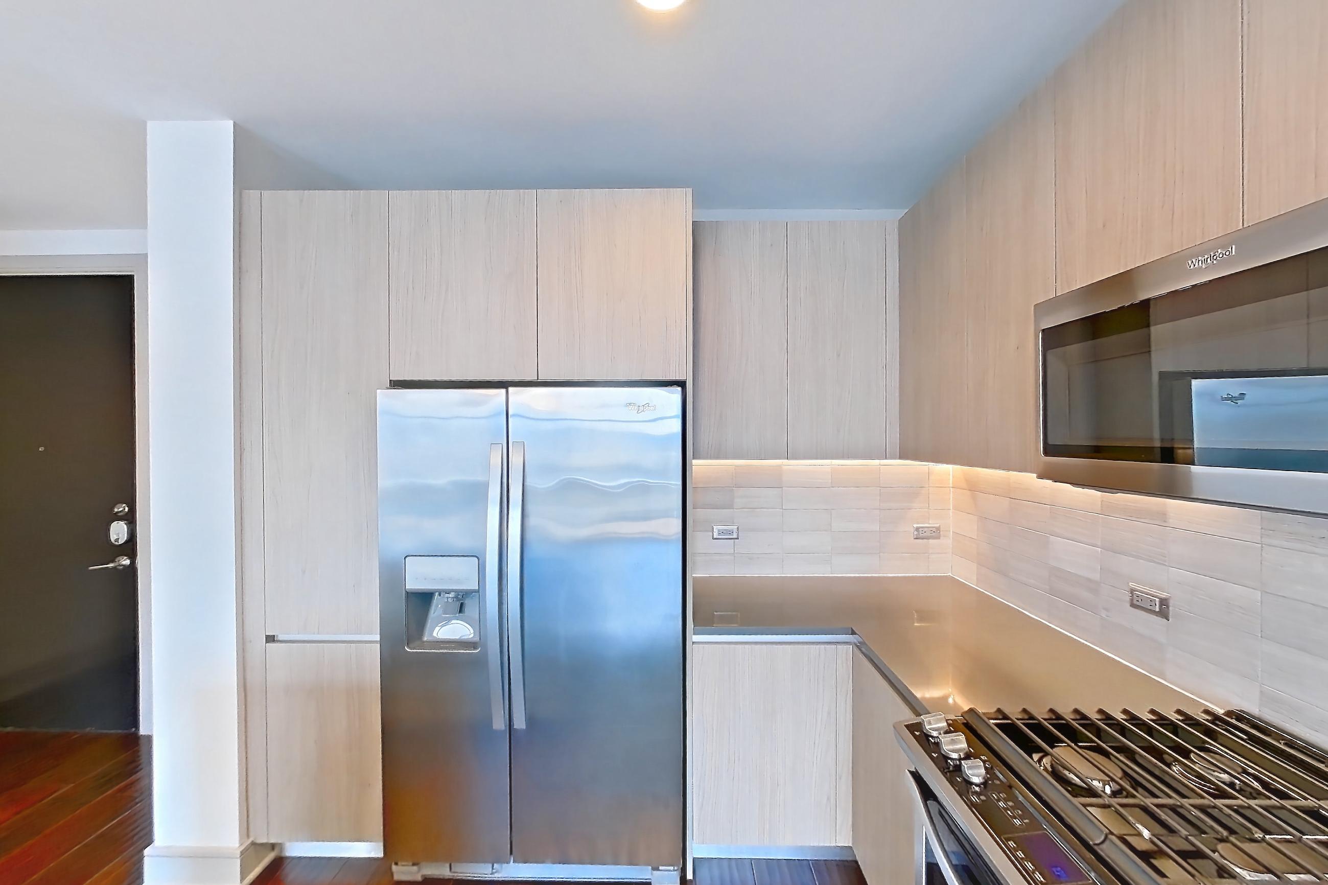 Kitchen with dark wood-finish flooring, gas range, light countertops, microwave, oven/range, refrigerator, stainless steel appliances, and water & ice dispenser, Apartment 1001 at Aris Market Square