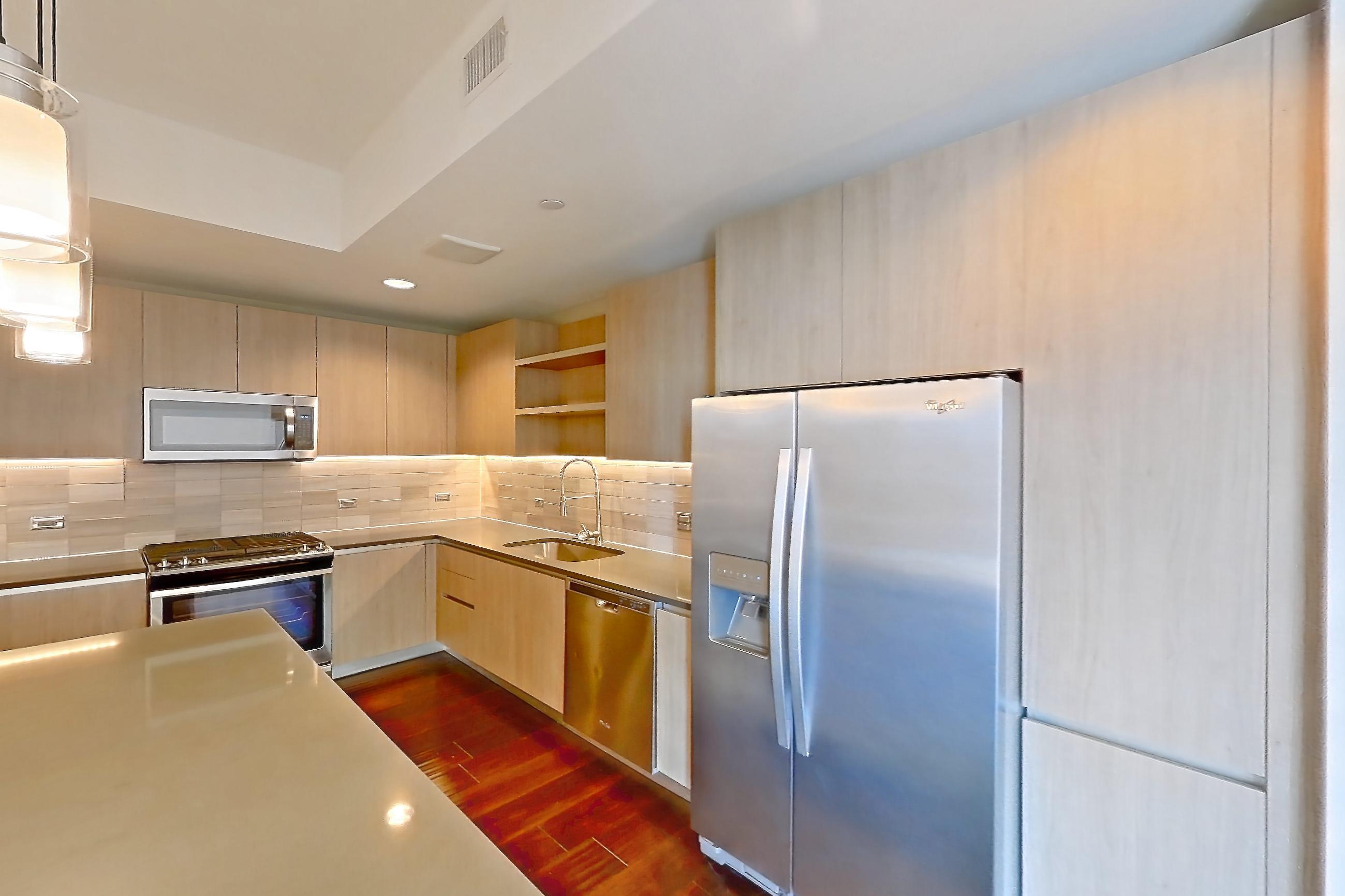 Kitchen space with dark wood-finish flooring, dishwasher, gas range, light countertops, oven/range, refrigerator, stainless steel appliances, and water & ice dispenser, Apartment 2512 at Aris Market Square
