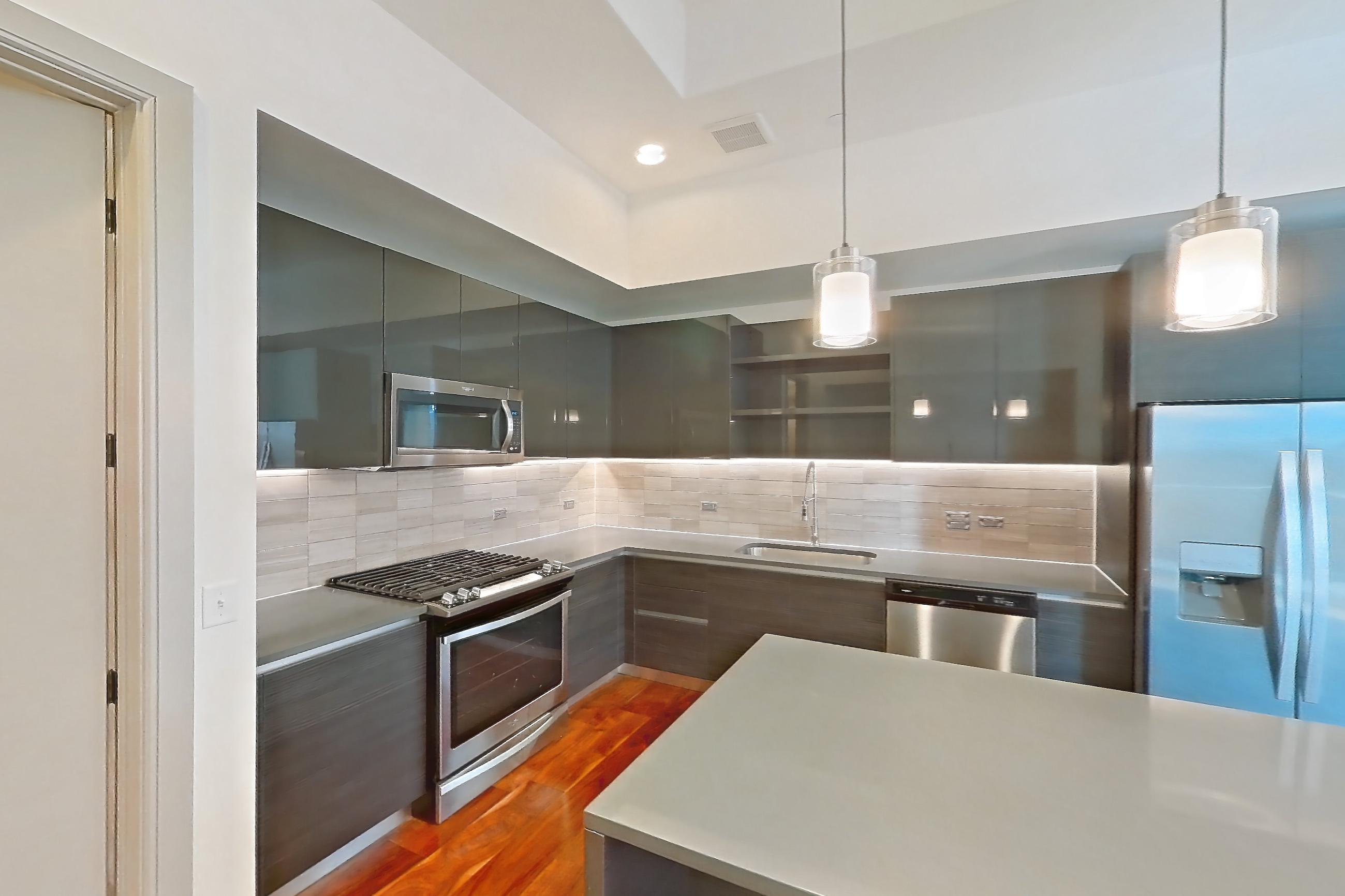 Kitchen space with dark wood-finish flooring, dishwasher, gas range, light countertops, oven/range, refrigerator, stainless steel appliances, water & ice dispenser, and wood-finish flooring, Apartment 3212 at Aris Market Square