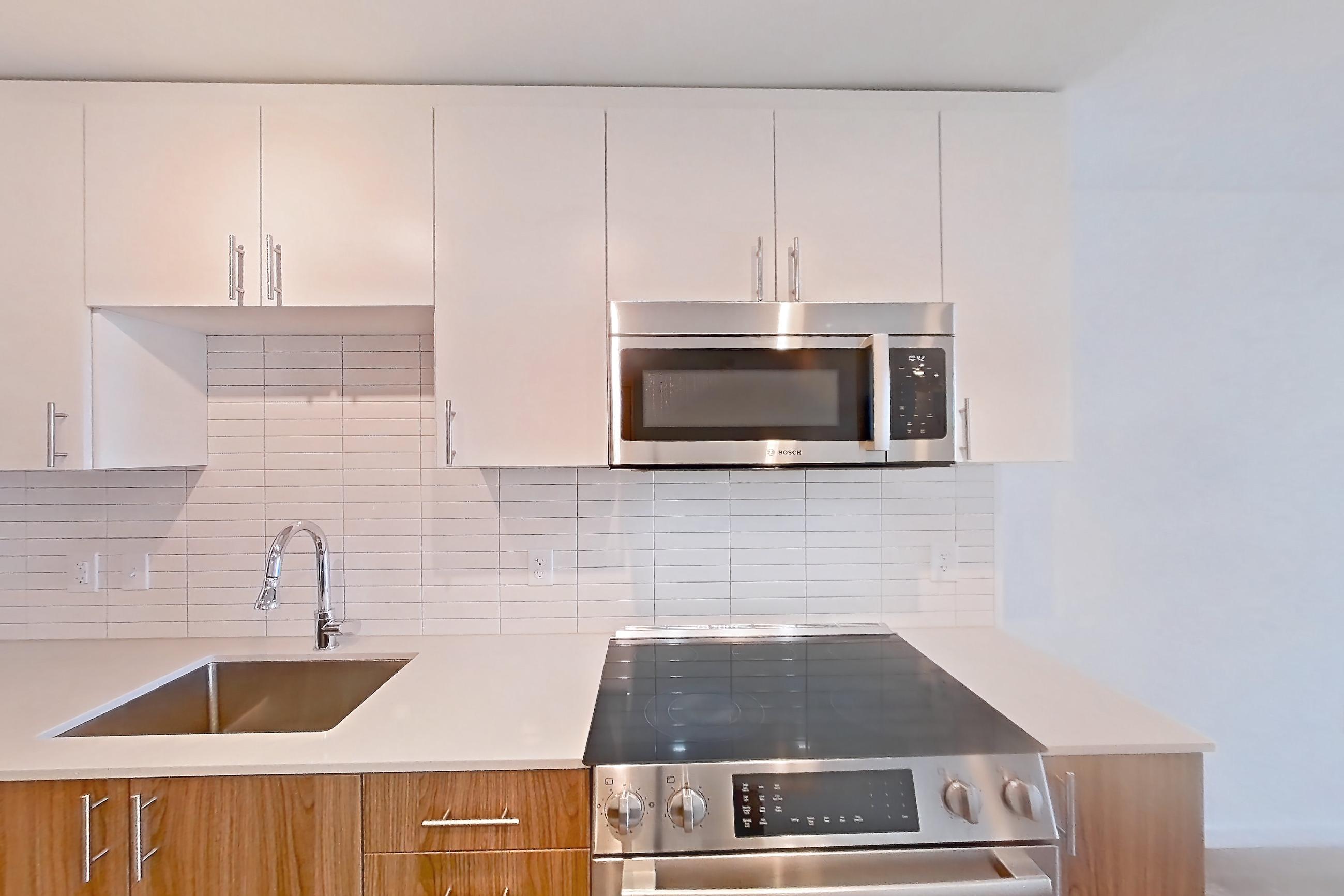 Kitchen with dishwasher, electric range, light countertops, light stone countertops, light wood-finish flooring, microwave, oven/range, refrigerator, and stainless steel appliances, Apartment 1111 at Cortland Rosslyn