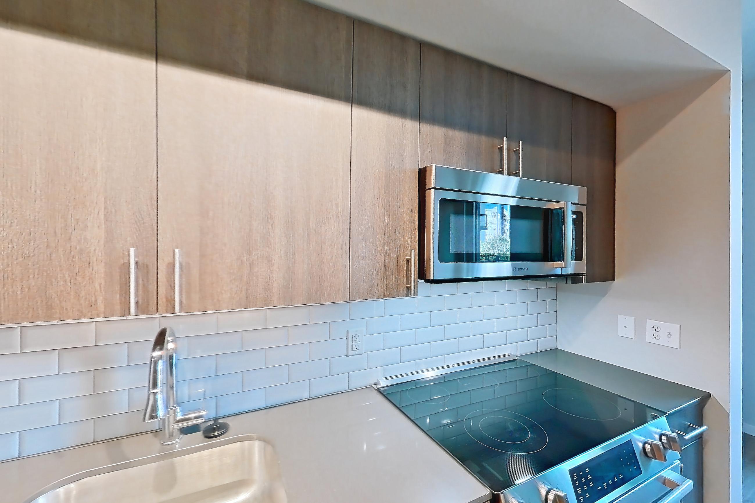Kitchen with dishwasher, electric range, light stone countertops, light wood-finish flooring, oven/range, refrigerator, and stainless steel appliances, Apartment 1-0310 at Cortland Rosslyn